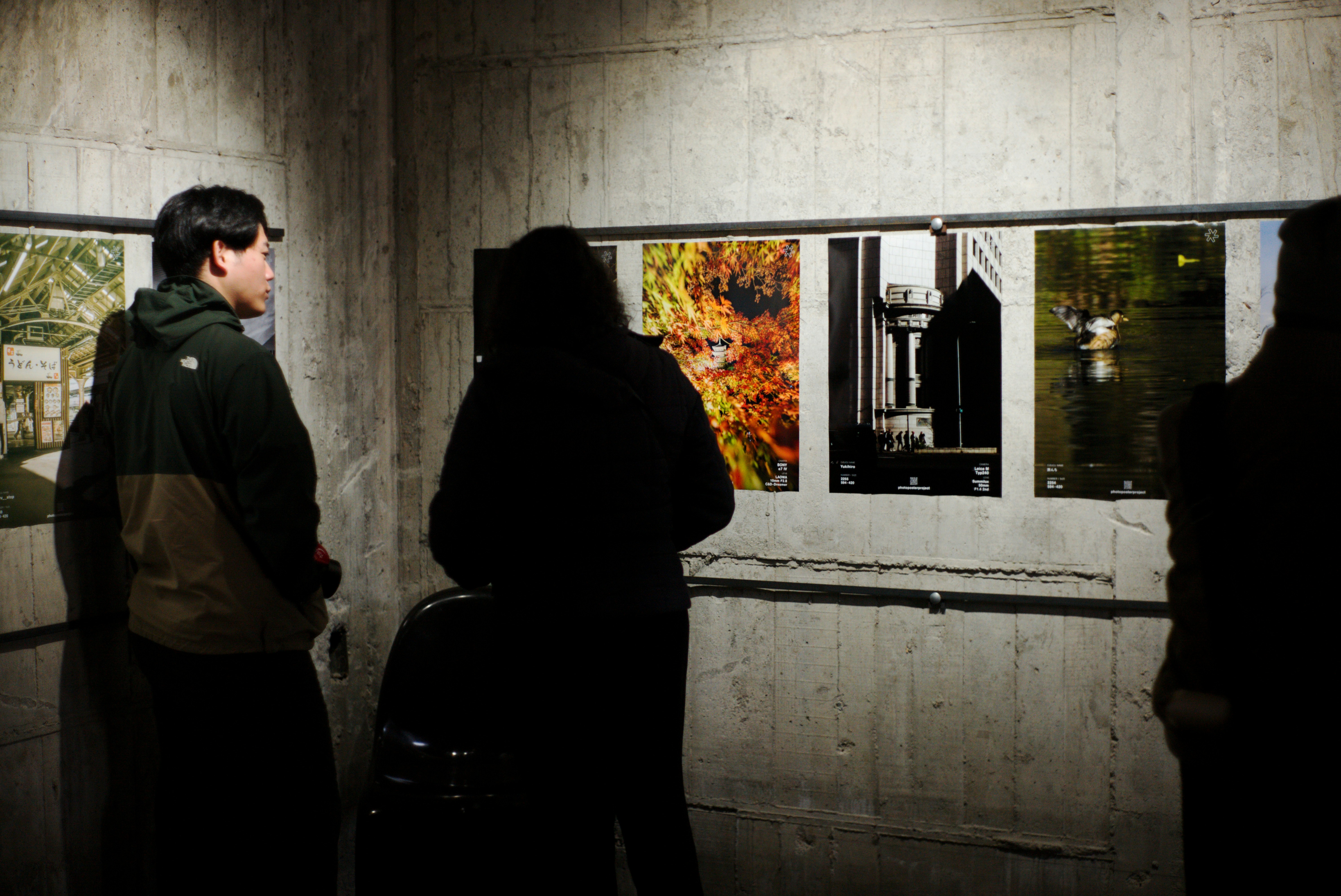 京都の壁面に並ぶ写真ポスターを見つめる人々のある展示空間