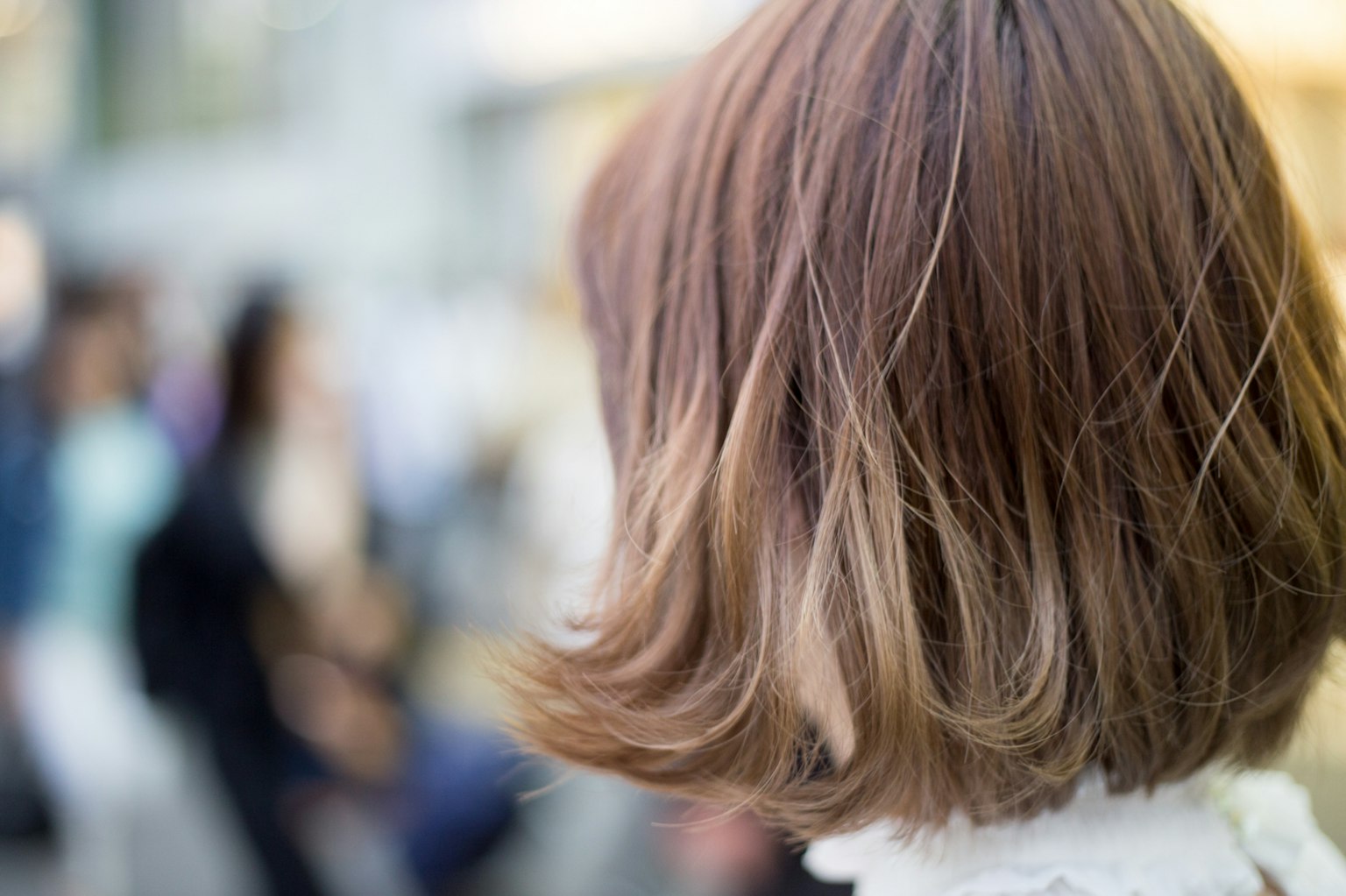 Mujer con cabello castaño vista desde atrás con personas al fondo