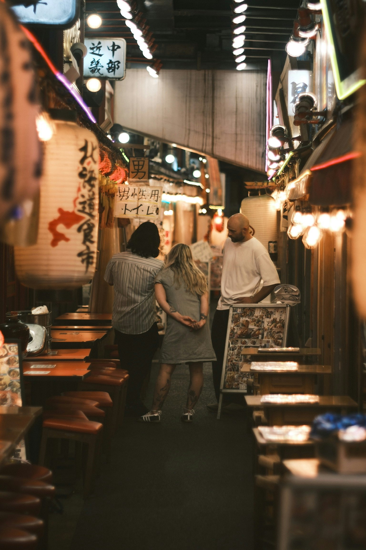 狭い路地にある日本の飲食店の風景 人々がメニューを見ている 明るい提灯と木製のテーブルが並ぶ