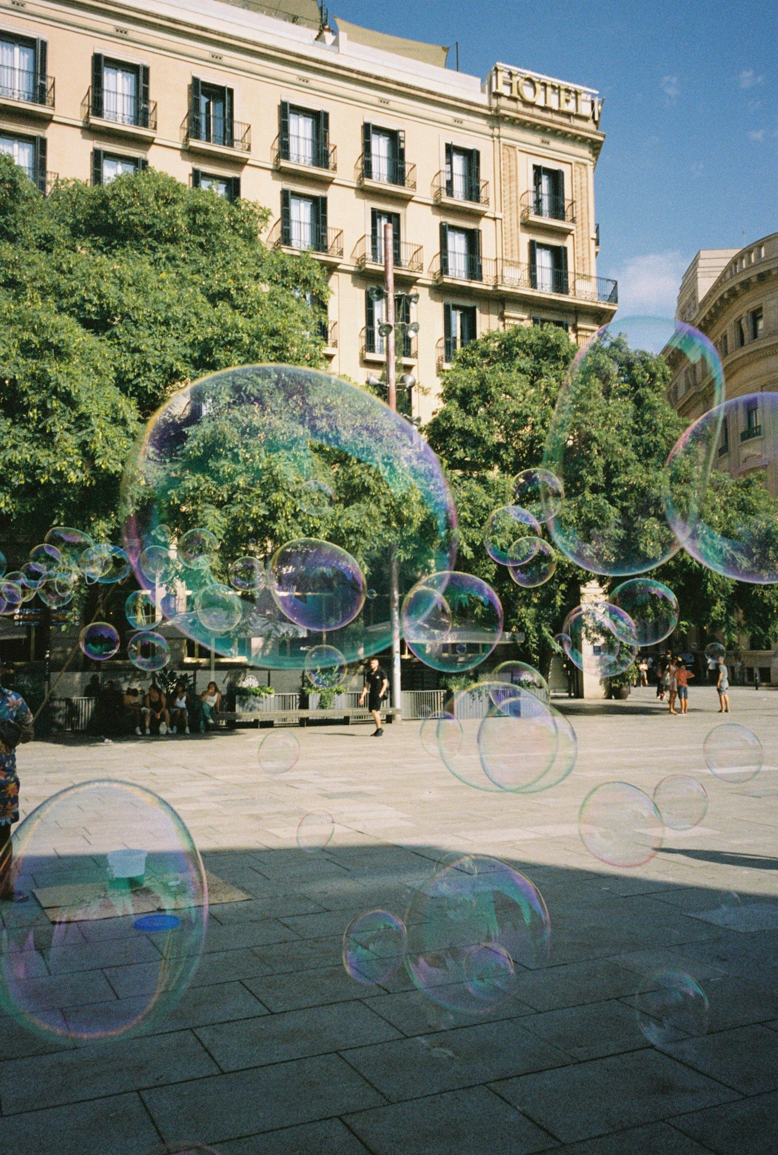 Grandi bolle di sapone che fluttuano in una piazza di Barcellona circondata da verde