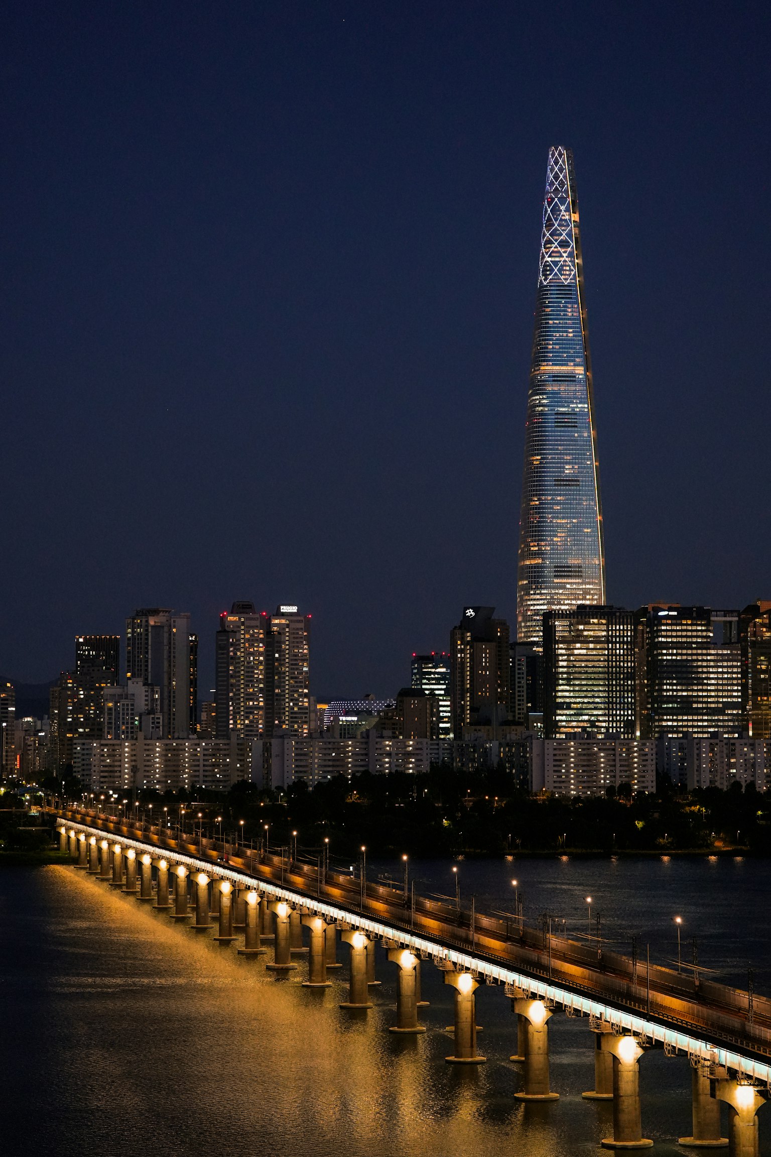 夜のソウルのスカイラインにそびえるロッテワールドタワーと光る橋