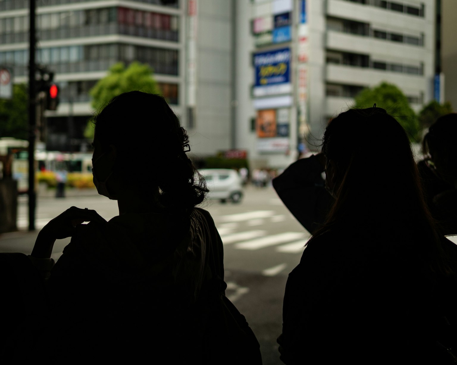 Silhouette di persone in attesa all'angolo di una strada con edifici sullo sfondo