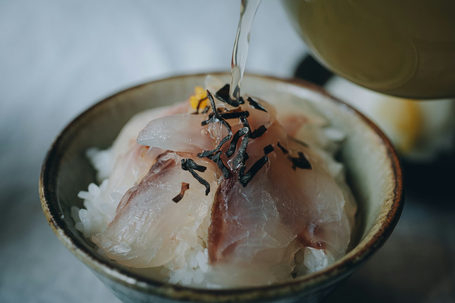 Un tazón de arroz cubierto con sashimi fresco mientras se le vierte caldo caliente
