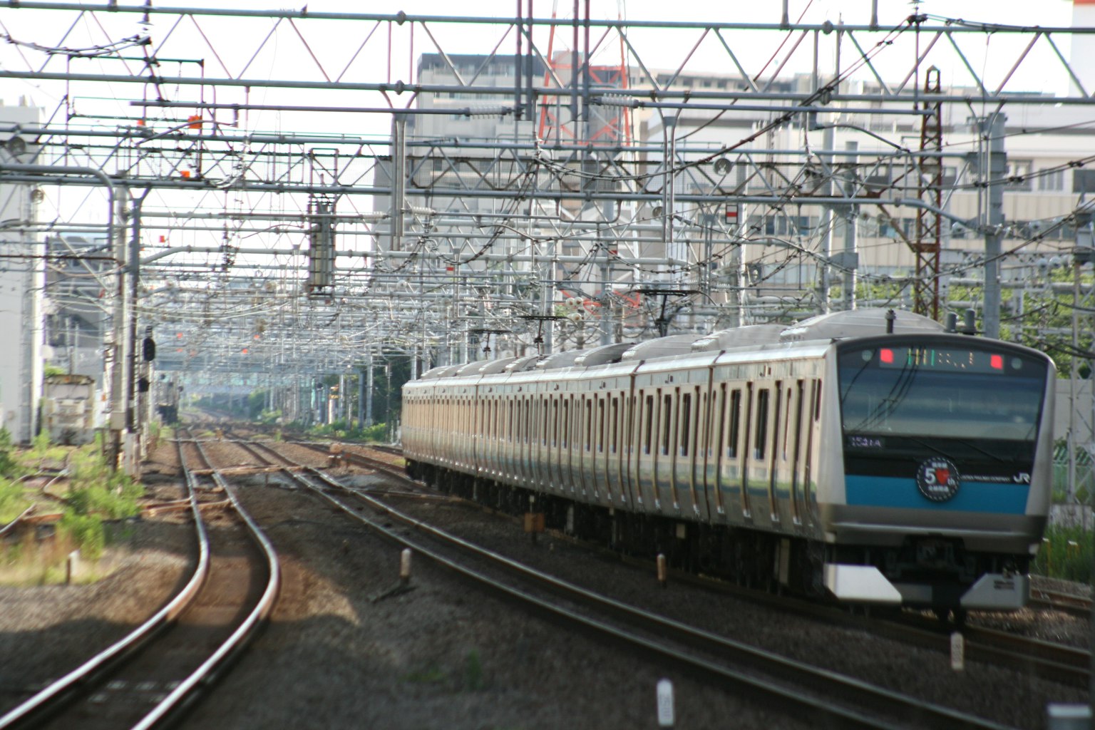 Un train circulant sur des voies avec des lignes aériennes et des bâtiments en arrière-plan