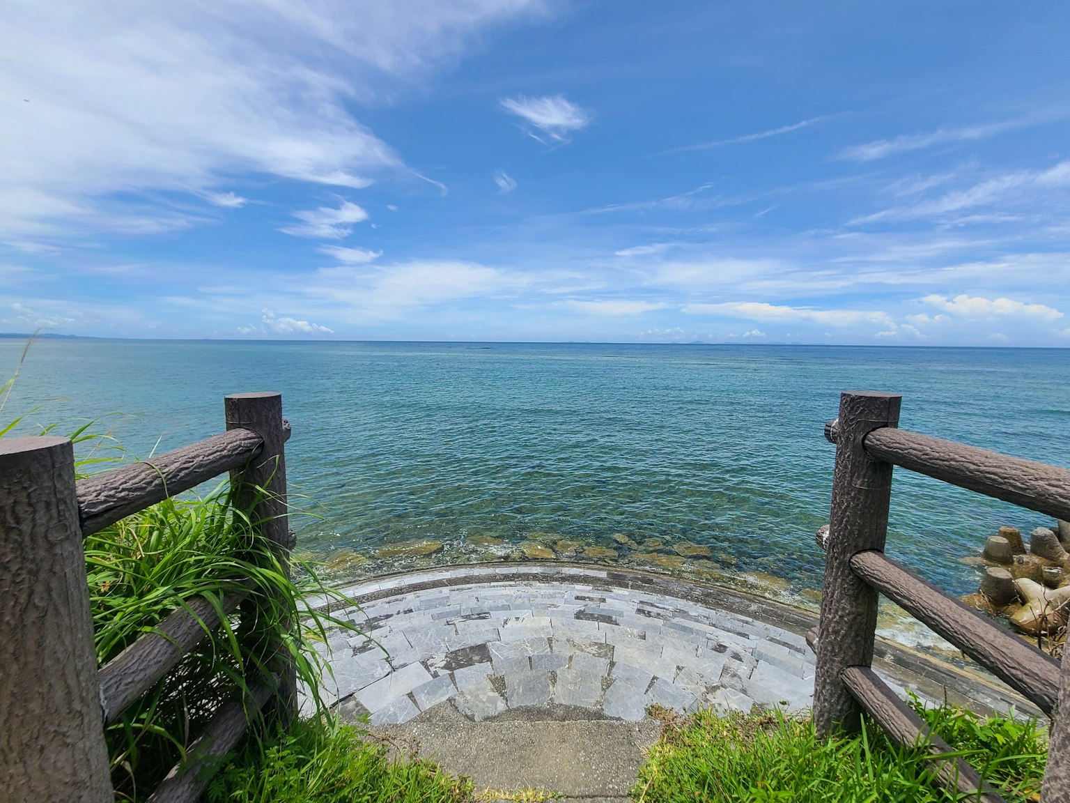 Vista del mare e del cielo blu con una terrazza circolare in pietra e una ringhiera in legno