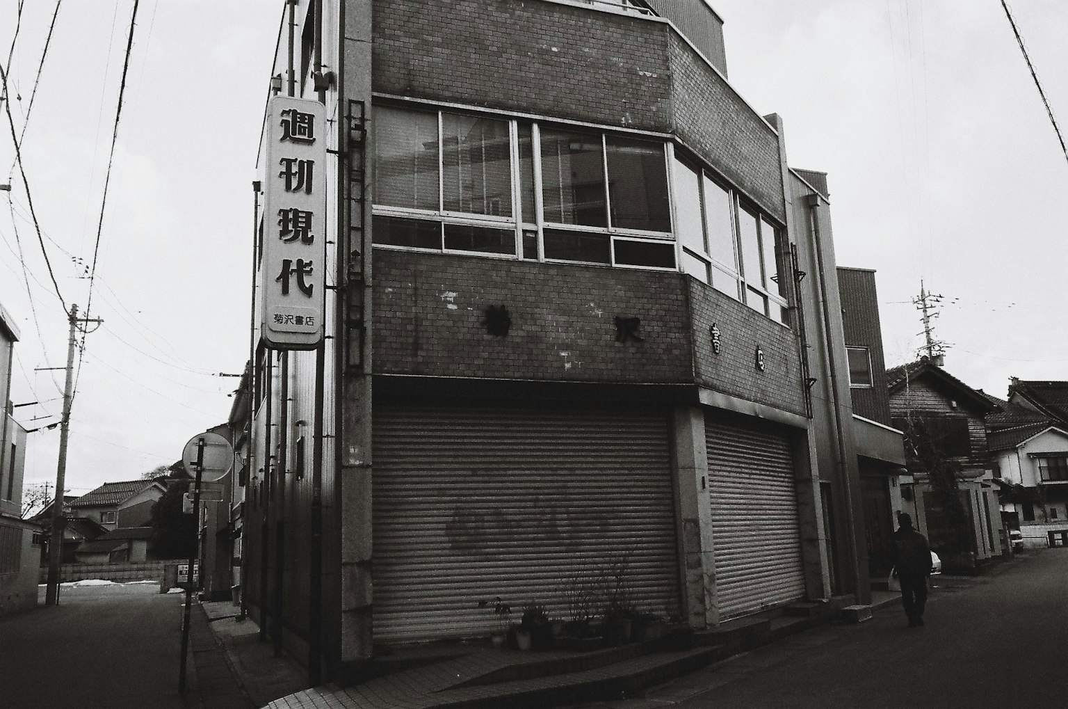 A gray building at the corner of an old street featuring windows and a shutter typical of Japanese architecture