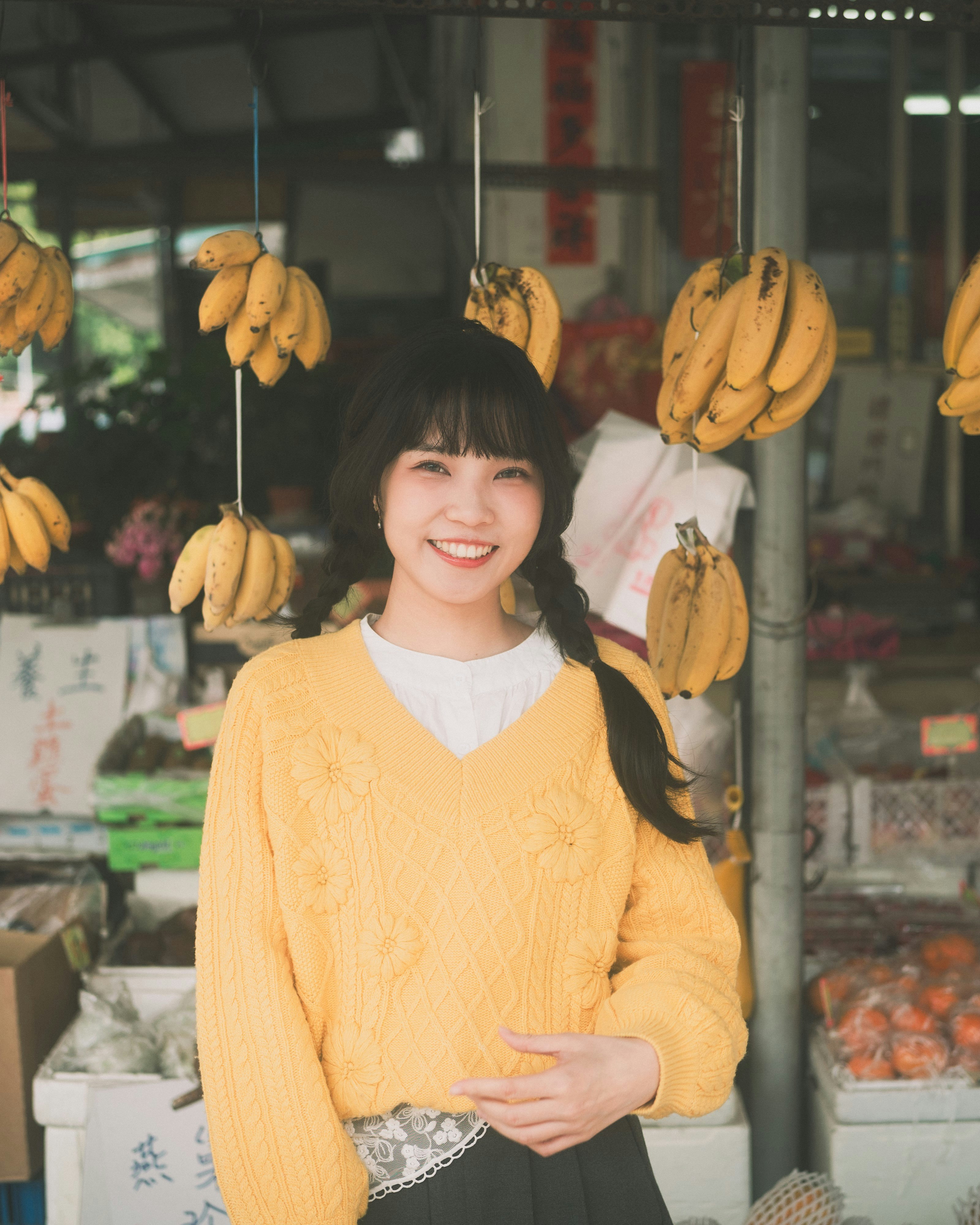 軒先に吊るされたバナナと笑顔の女性のいる果物店