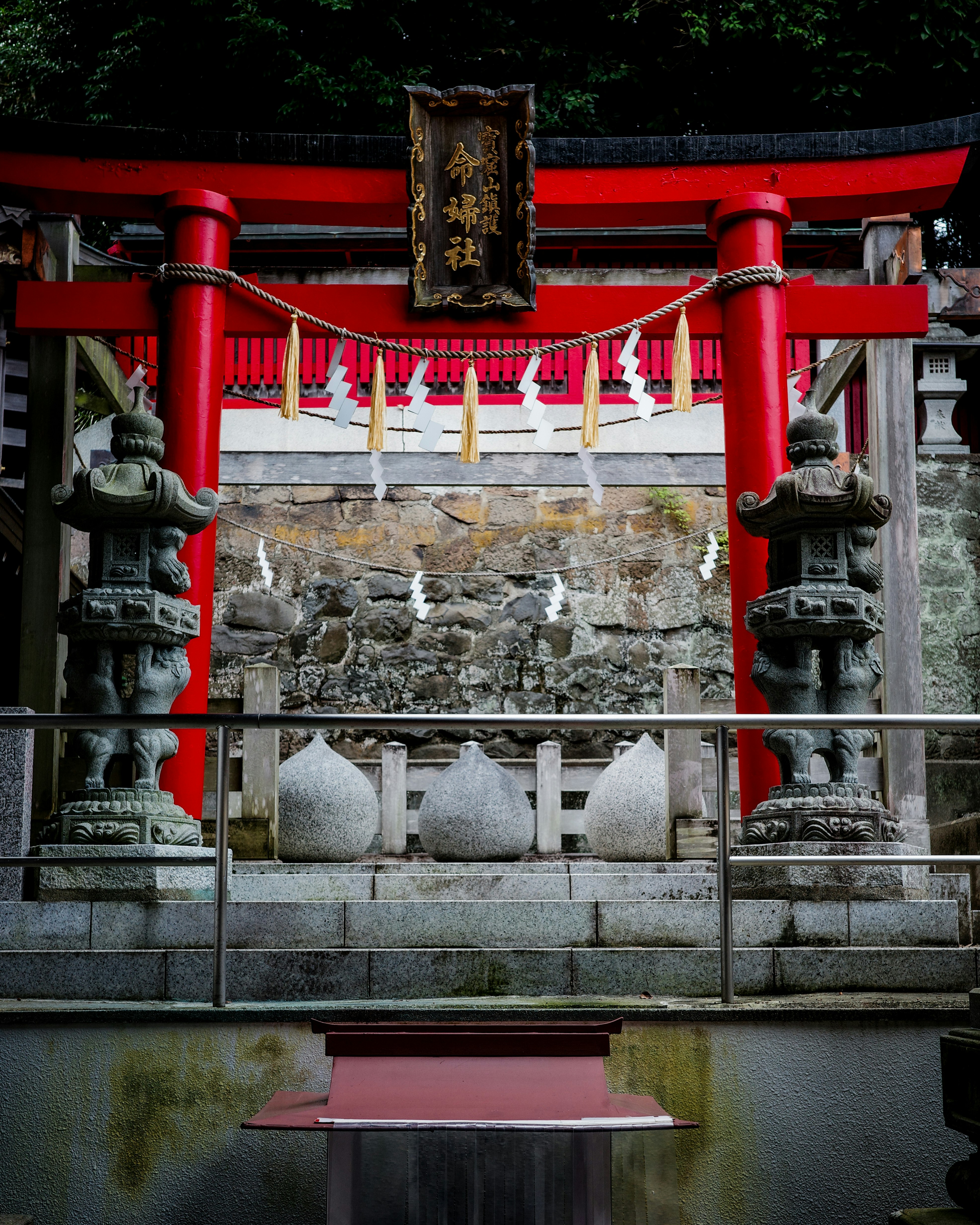 Zona de oración en un santuario sintoísta con un torii rojo y escalones de piedra