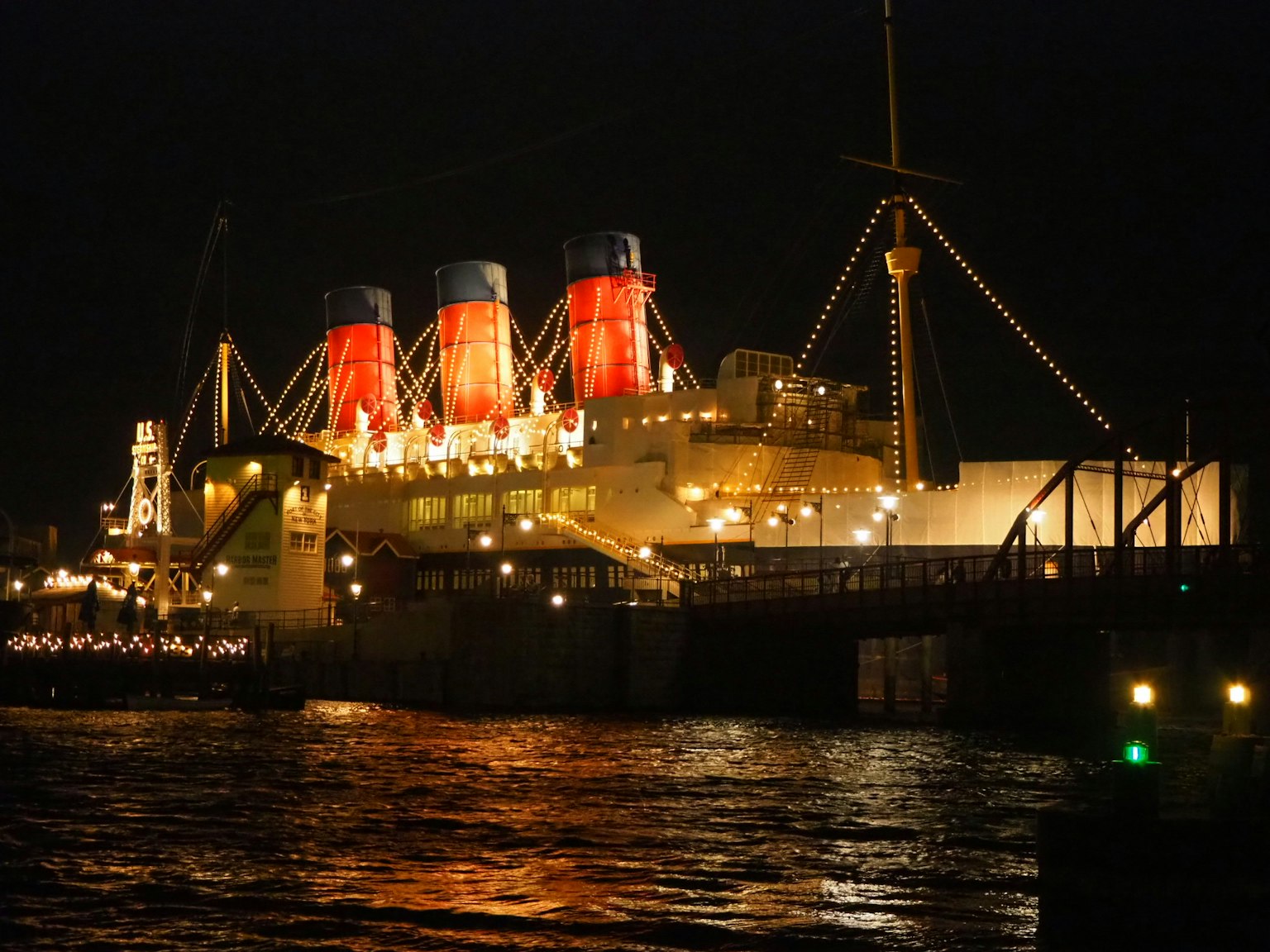 Beleuchtetes Luxuskreuzfahrtschiff bei Nacht mit roten Schornsteinen