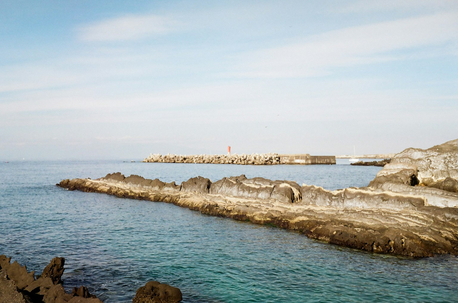 Laut tenang dan pemandangan berbatu dengan dermaga yang aus di latar belakang