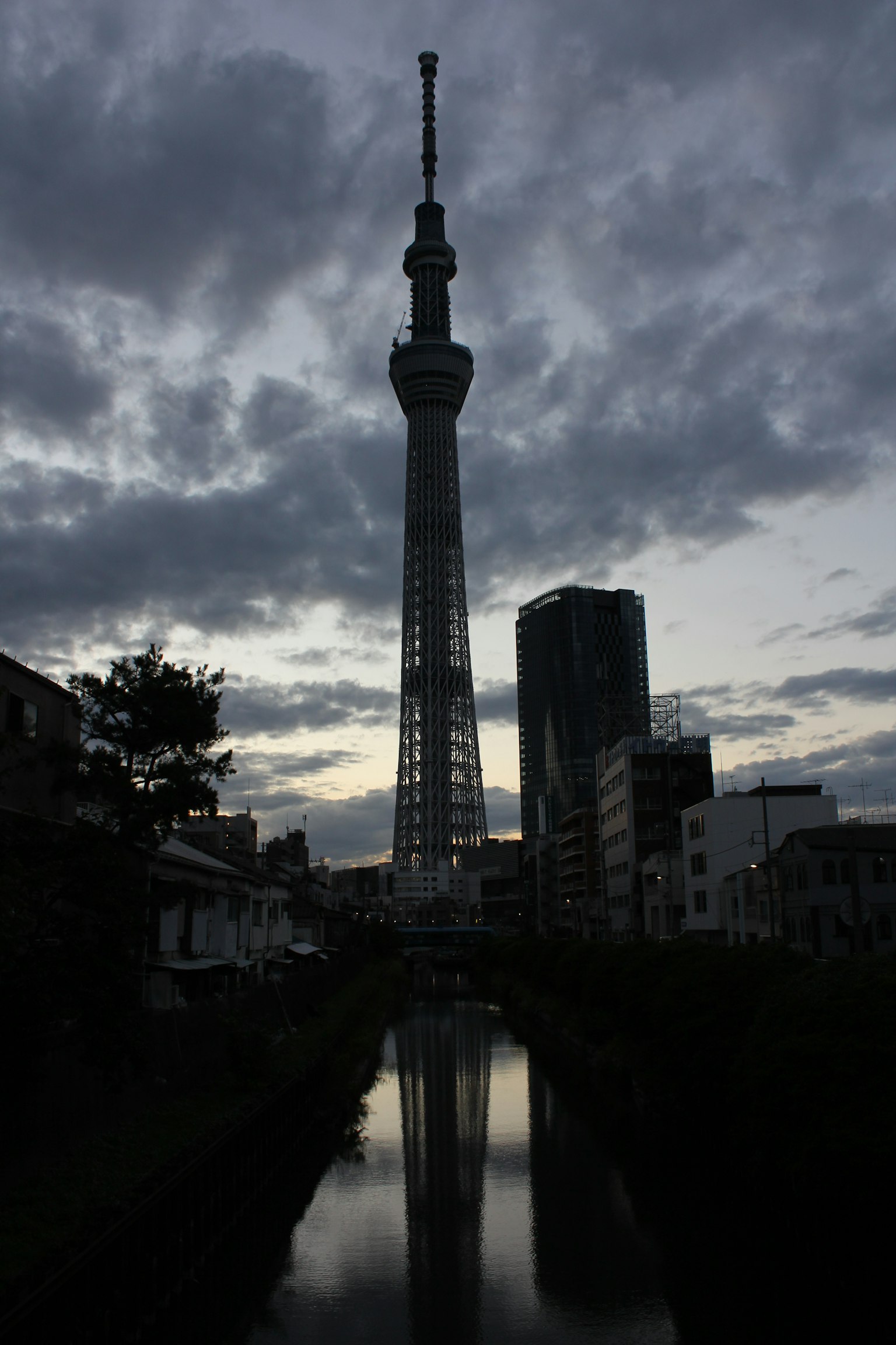 Tokyo Skytree im Silhouetten gegen einen bewölkten Himmel mit Wasserreflexion