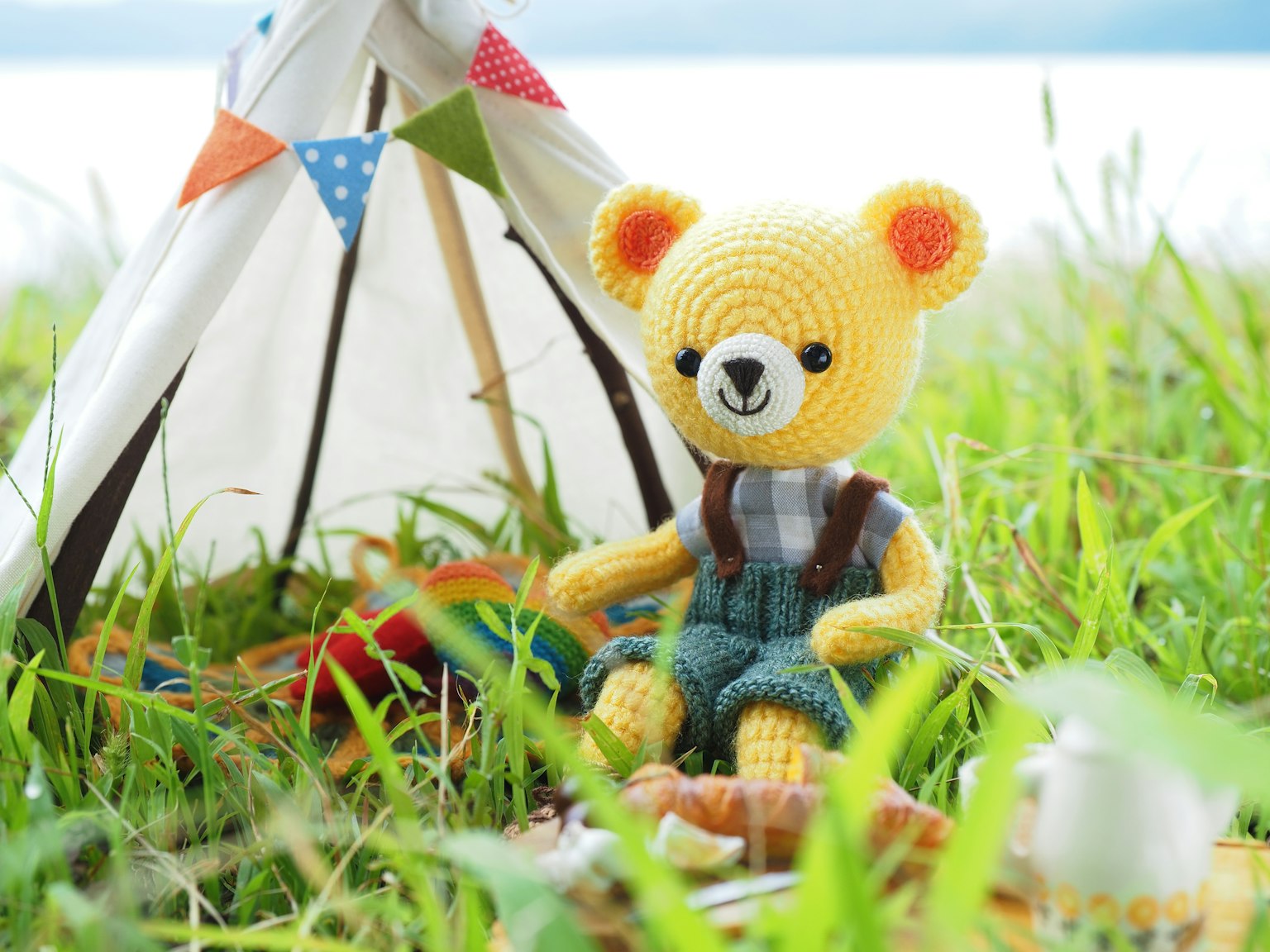 Un ours en peluche jaune assis devant une tente au milieu de l'herbe verte