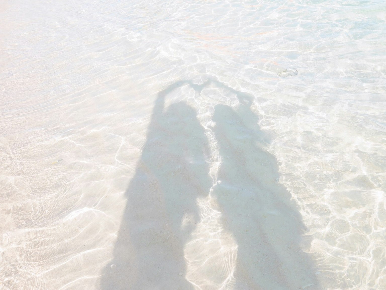 Schatten von zwei Personen, die eine Herzform im flachen Wasser bilden