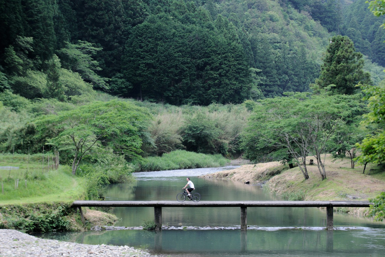 緑豊かな山々に囲まれた小川にかかる木製の橋を渡る人