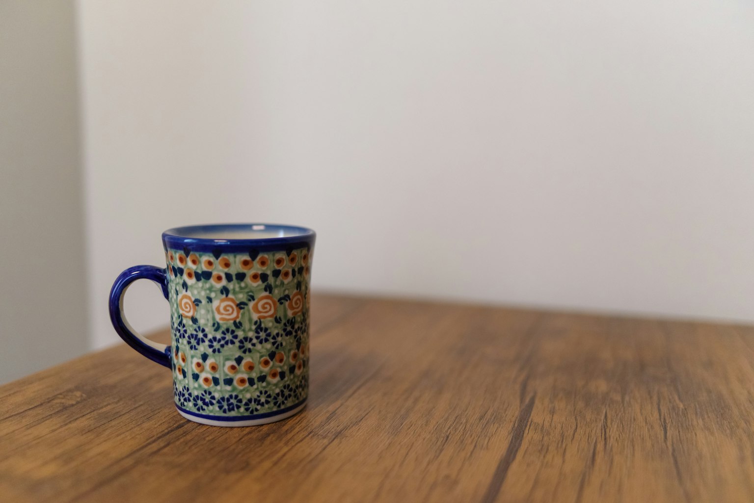 Una taza de diseño azul y naranja colocada sobre una mesa de madera
