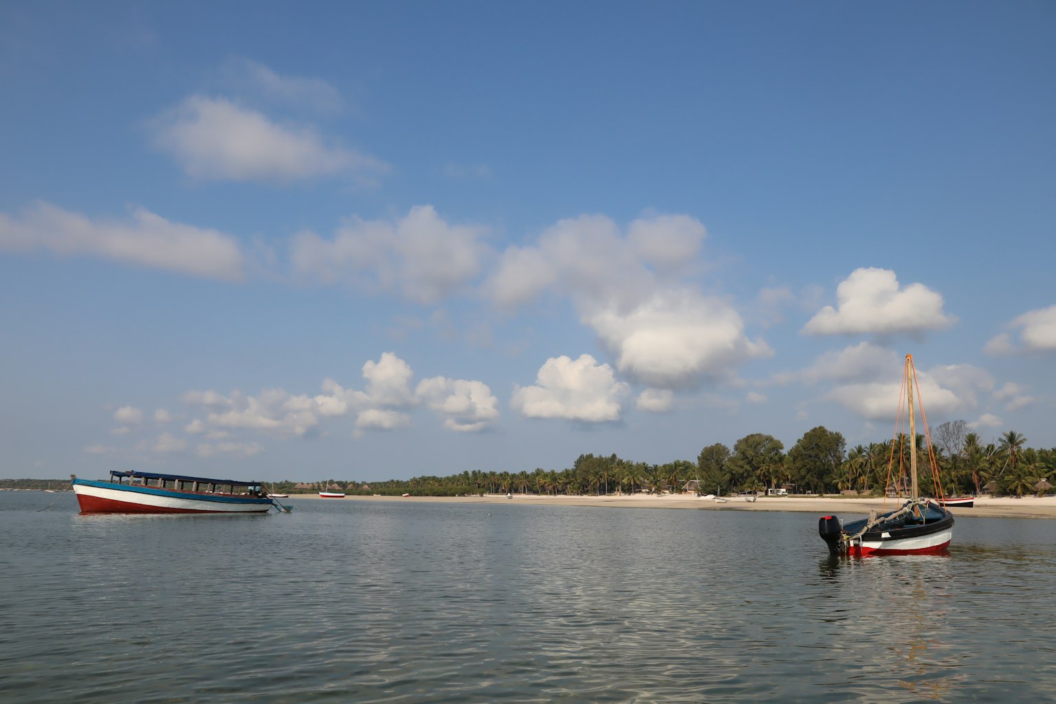 Paisaje marino sereno con dos botes en agua tranquila bajo un cielo azul y nubes esponjosas
