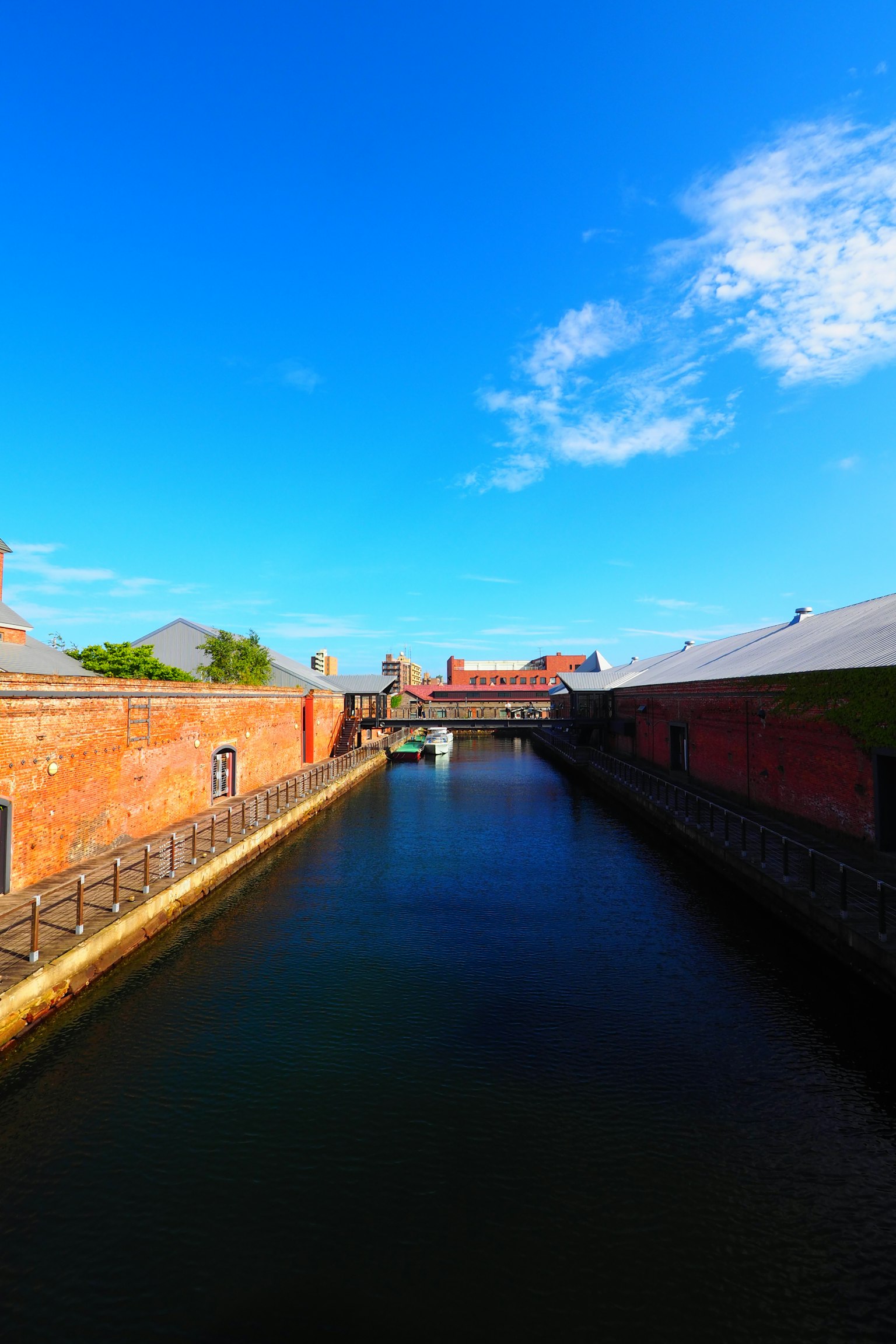 Un canal serein coulant entre des bâtiments en briques rouges sous un ciel bleu avec des nuages épars