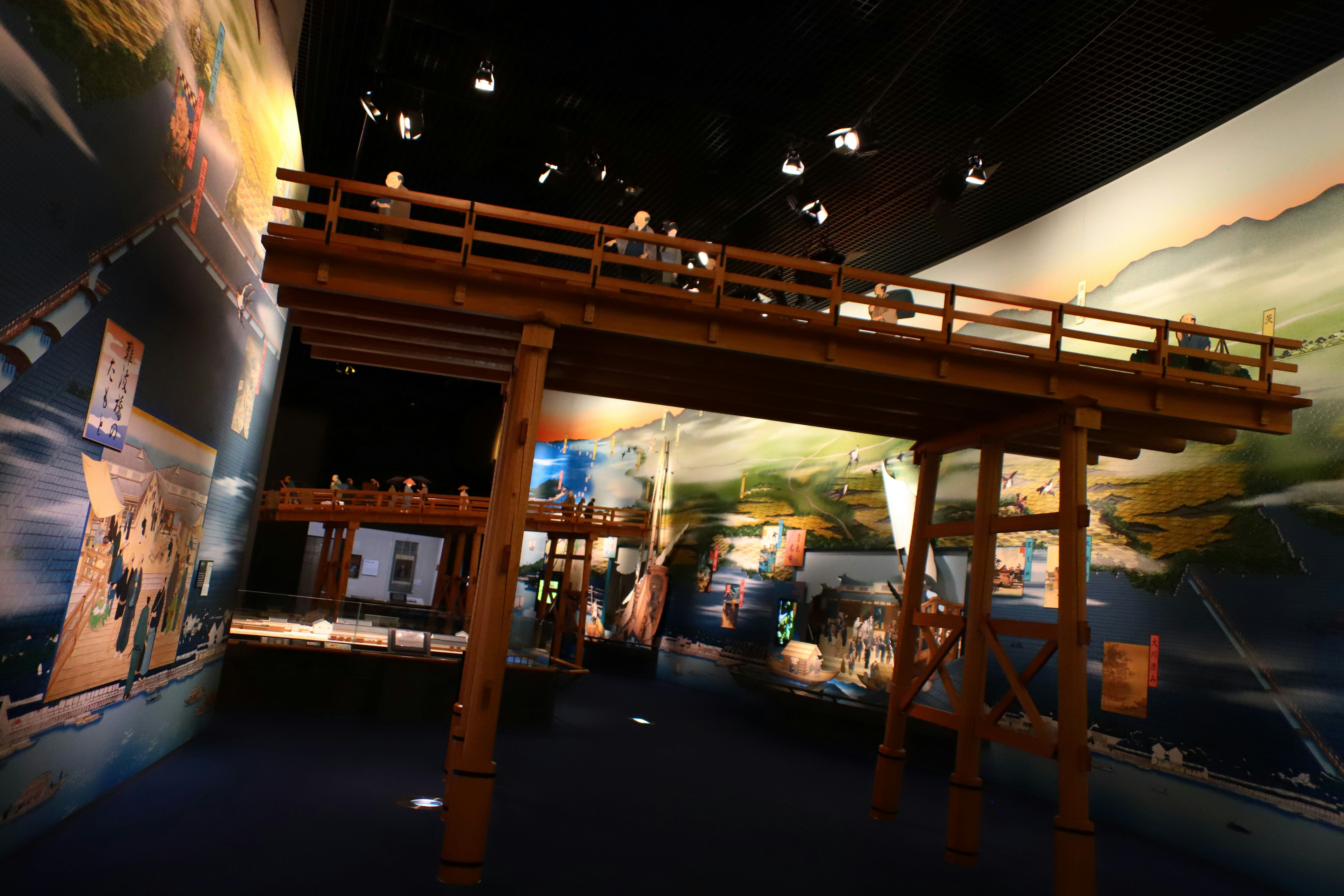 Außen-Ausstellungsbereich bei Nacht mit beleuchtetem Holzsteg und Ausstellungstafeln