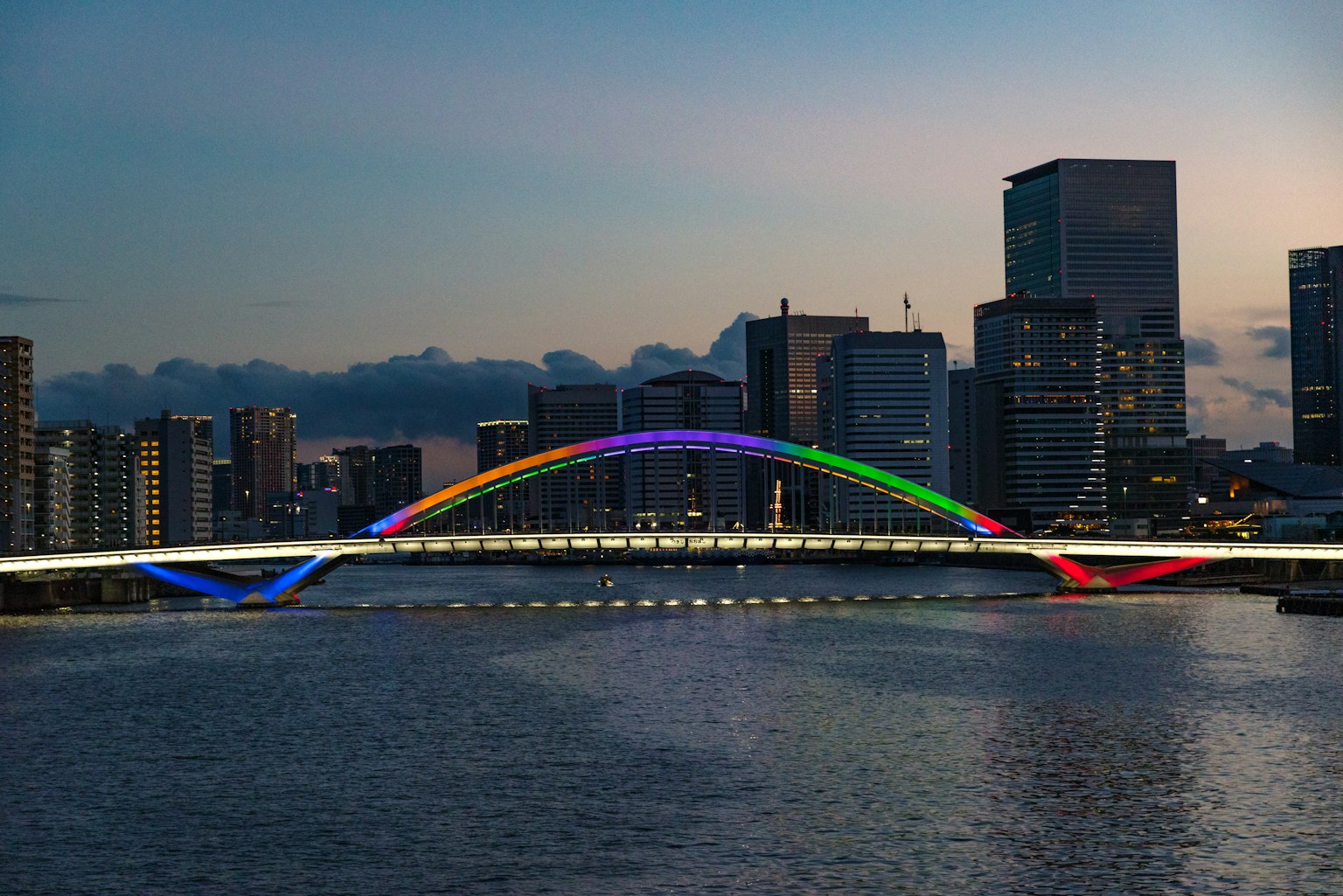 Ponte colorato arcobaleno illuminato al crepuscolo con skyline cittadino