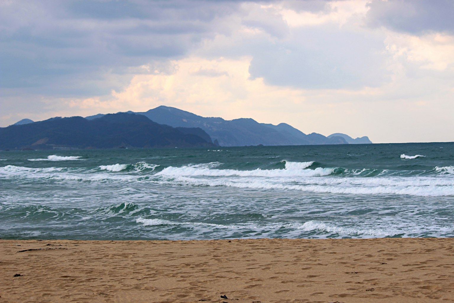 海岸景觀，海浪拍打海岸，遠處有山脈
