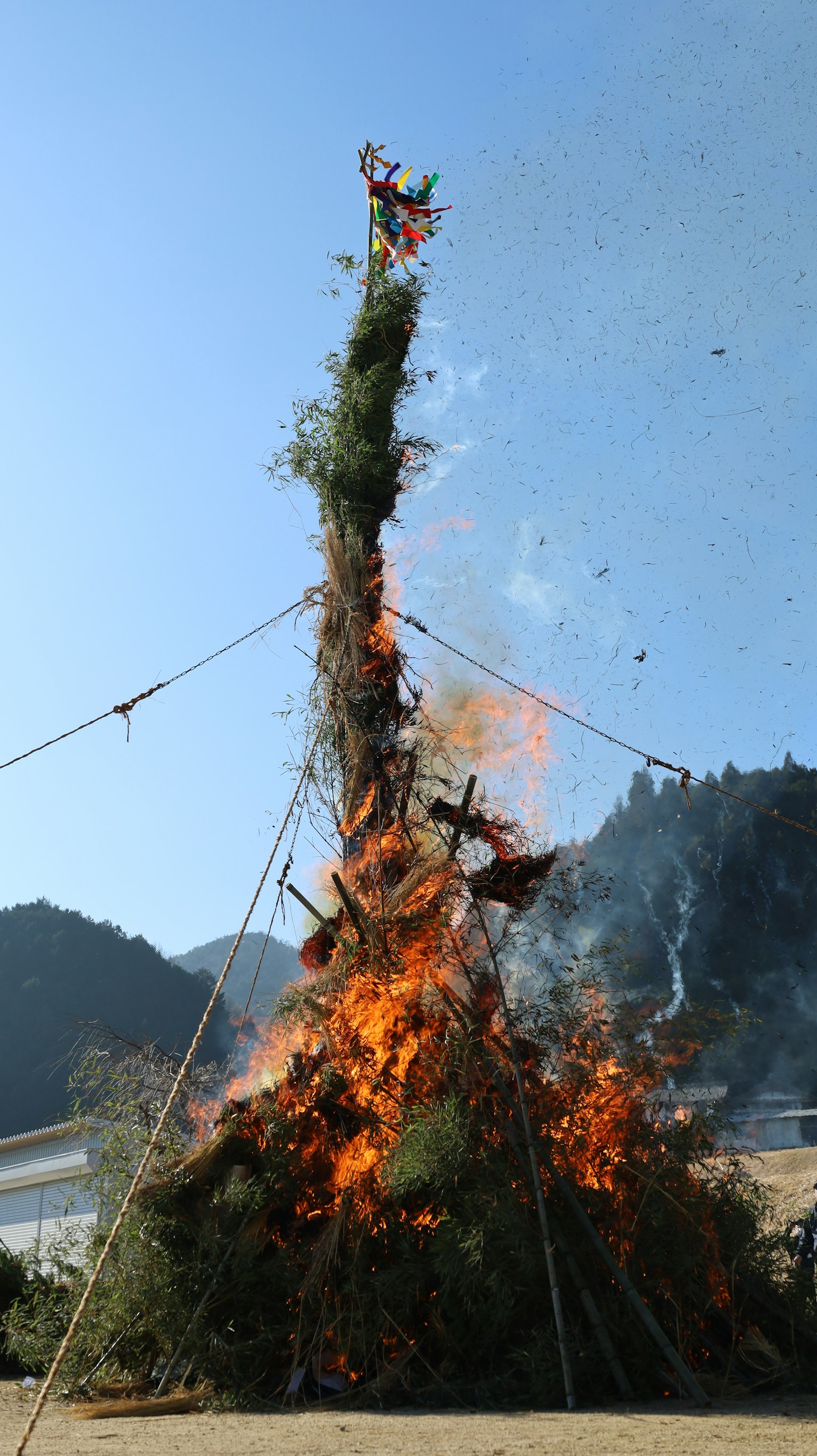 Ein großes Feuer brennt mit Grün und Flammen vor einer bergigen Kulisse