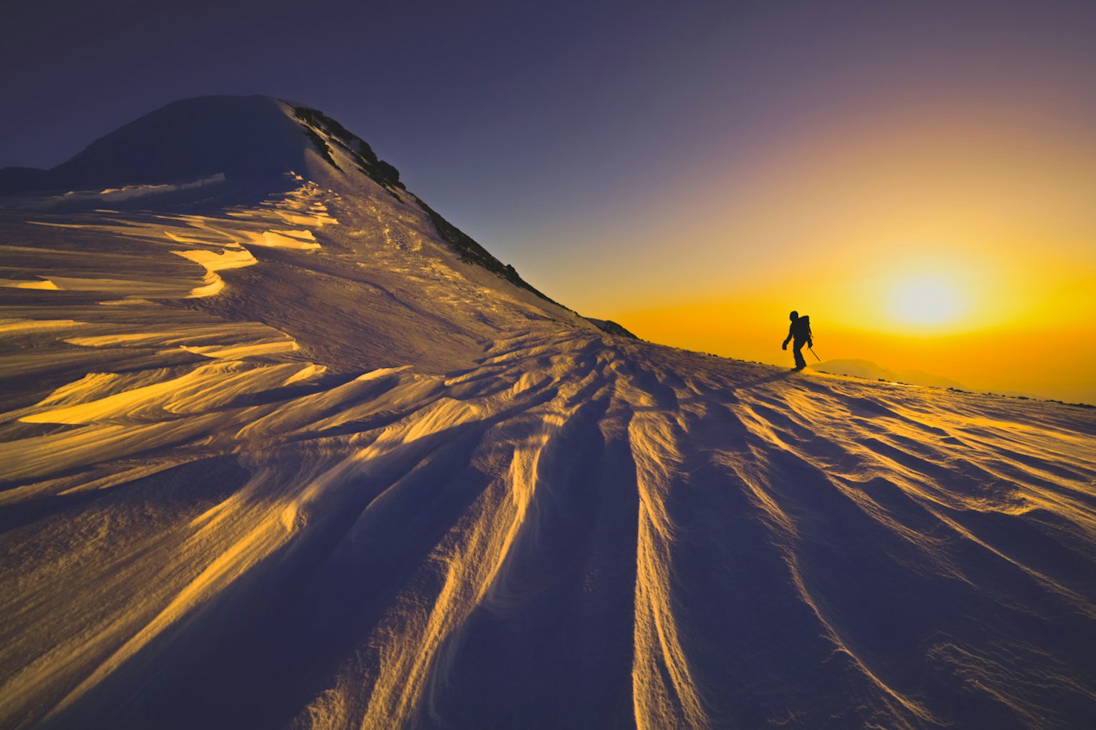 Climber ascending a snowy mountain slope with a stunning sunset