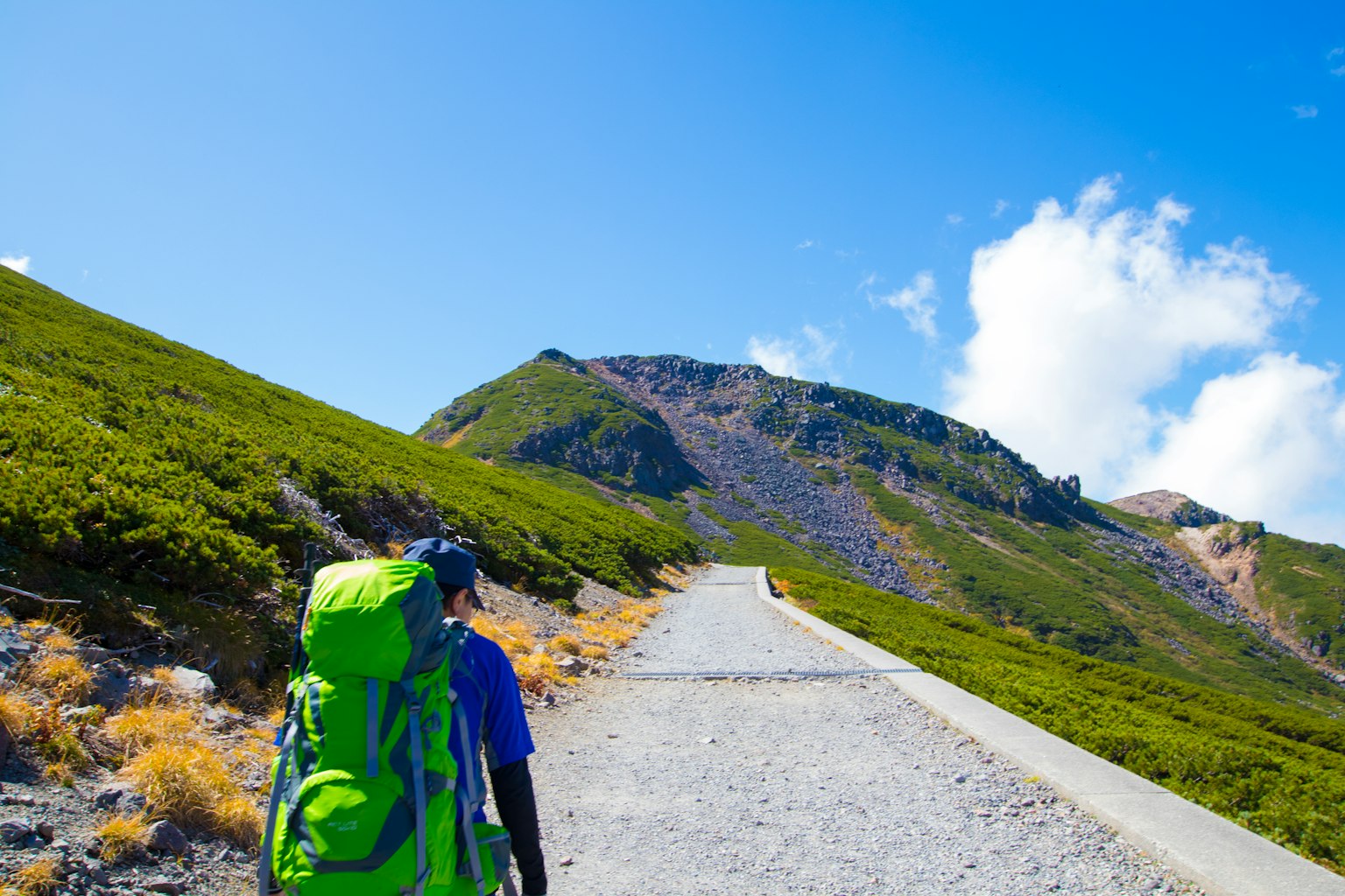 Pendaki dengan ransel hijau berjalan di jalur gunung