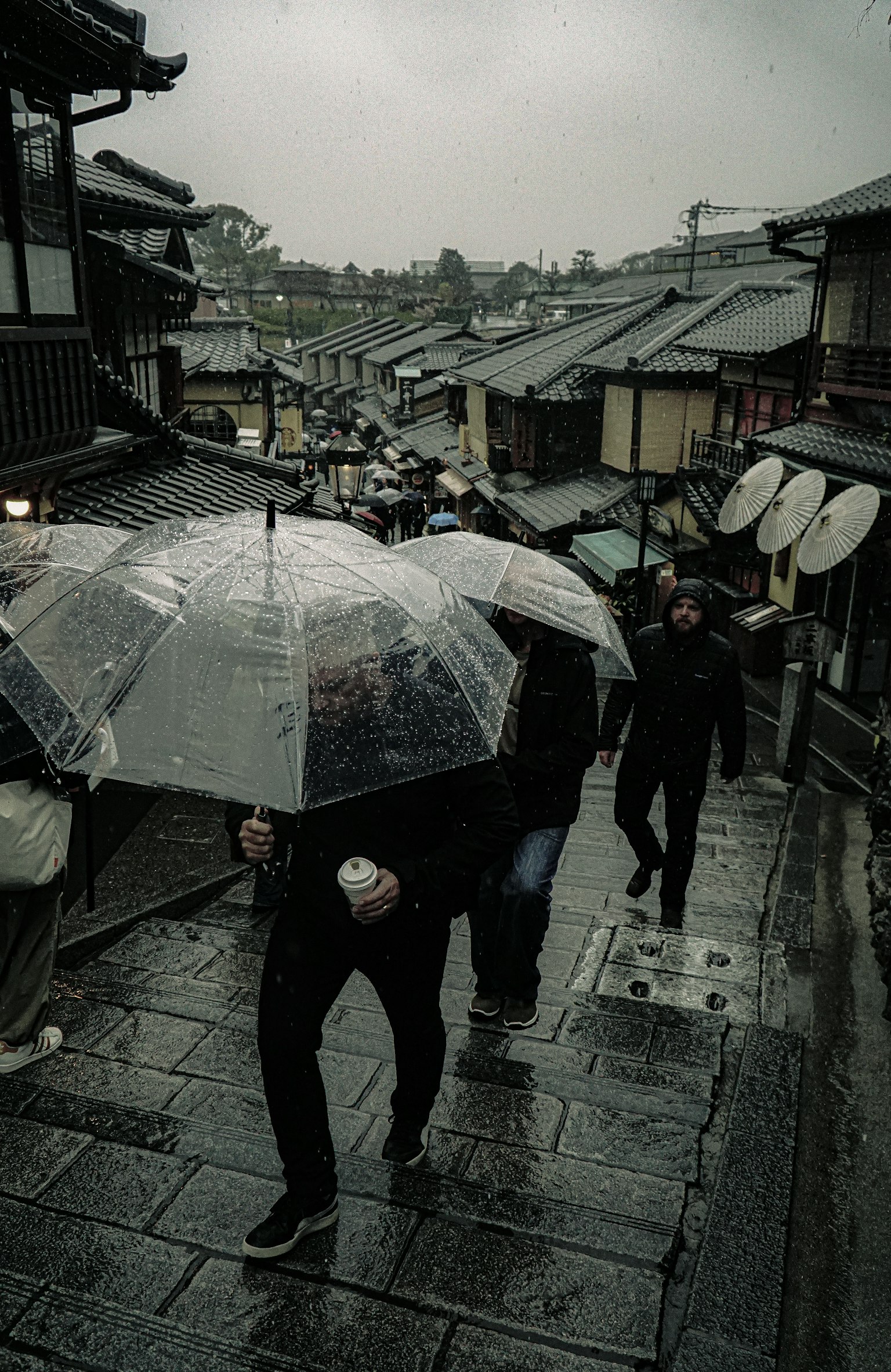 ผู้คนเดินใต้ร่มในฝนพร้อมวิวอาคารแบบดั้งเดิม