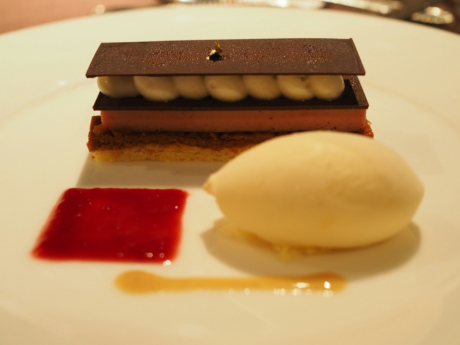An elegant dessert plate featuring a chocolate cake, vanilla ice cream, raspberry sauce, and caramel sauce