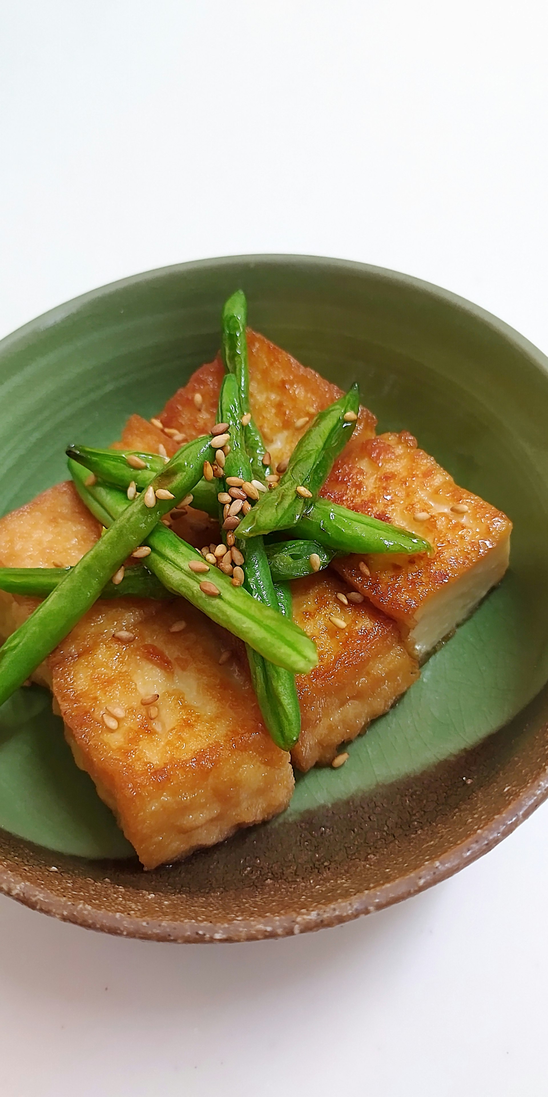 青い皿に盛られた揚げ豆腐に緑の野菜とごまがトッピングされた料理