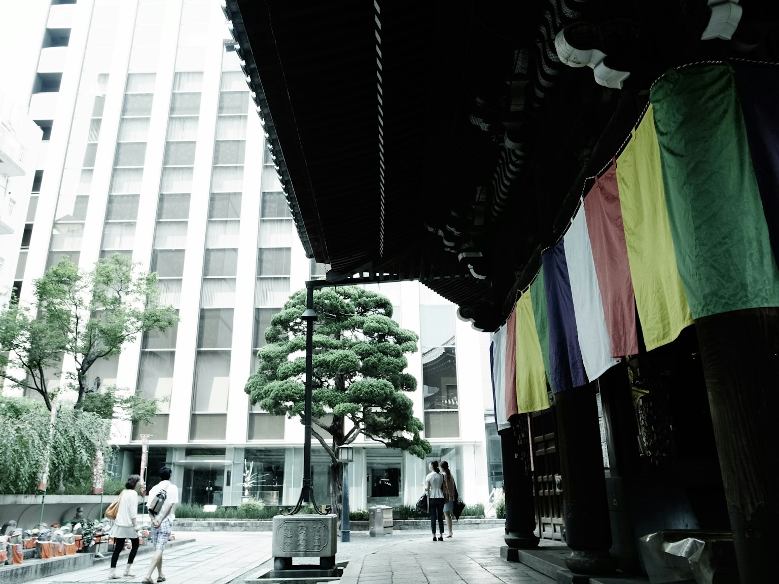 Traditional temple area in a modern city colorful banners hanging from pillars green tree in view