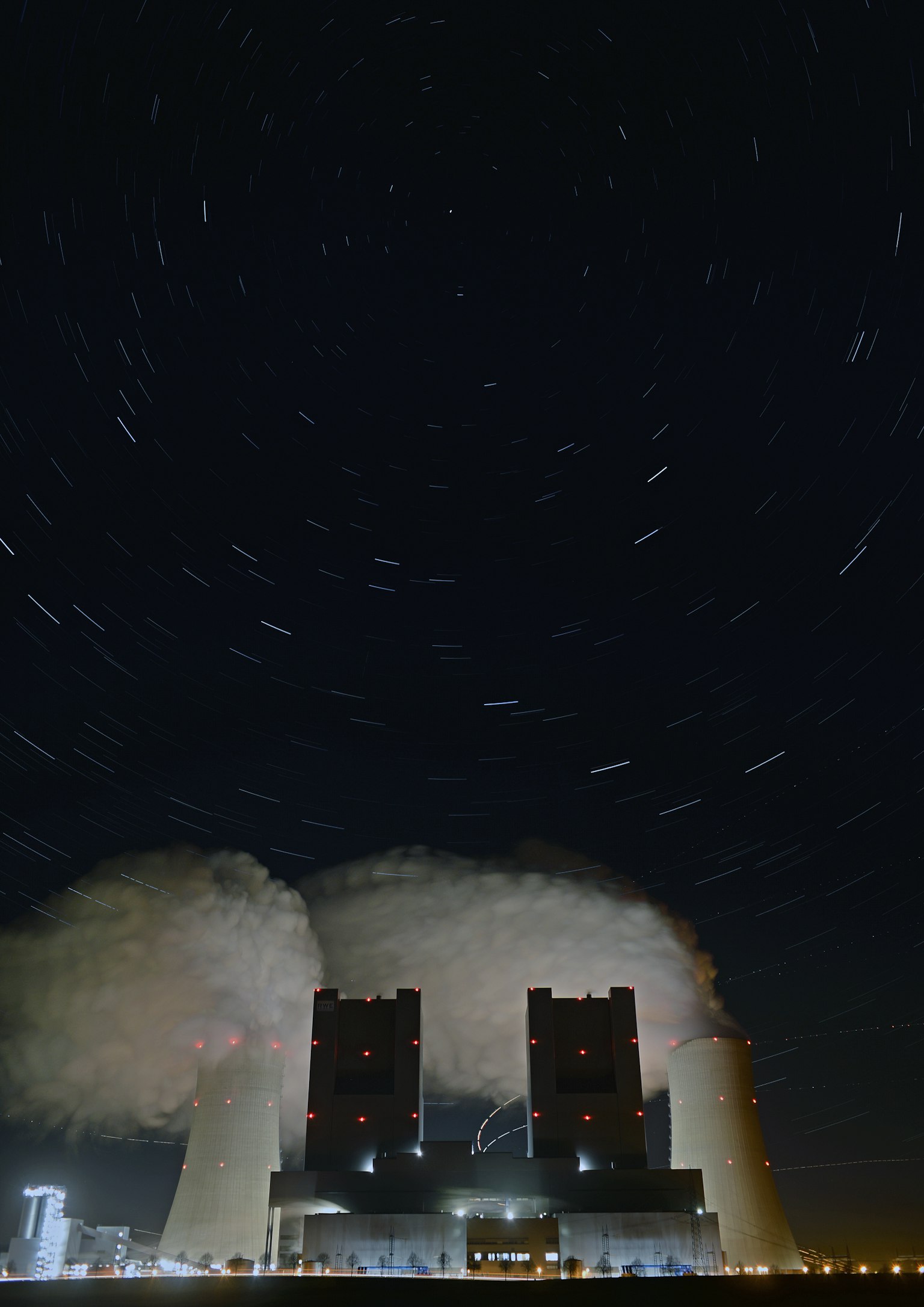 Centrale électrique avec des tours de refroidissement émettant de la vapeur sous un ciel étoilé