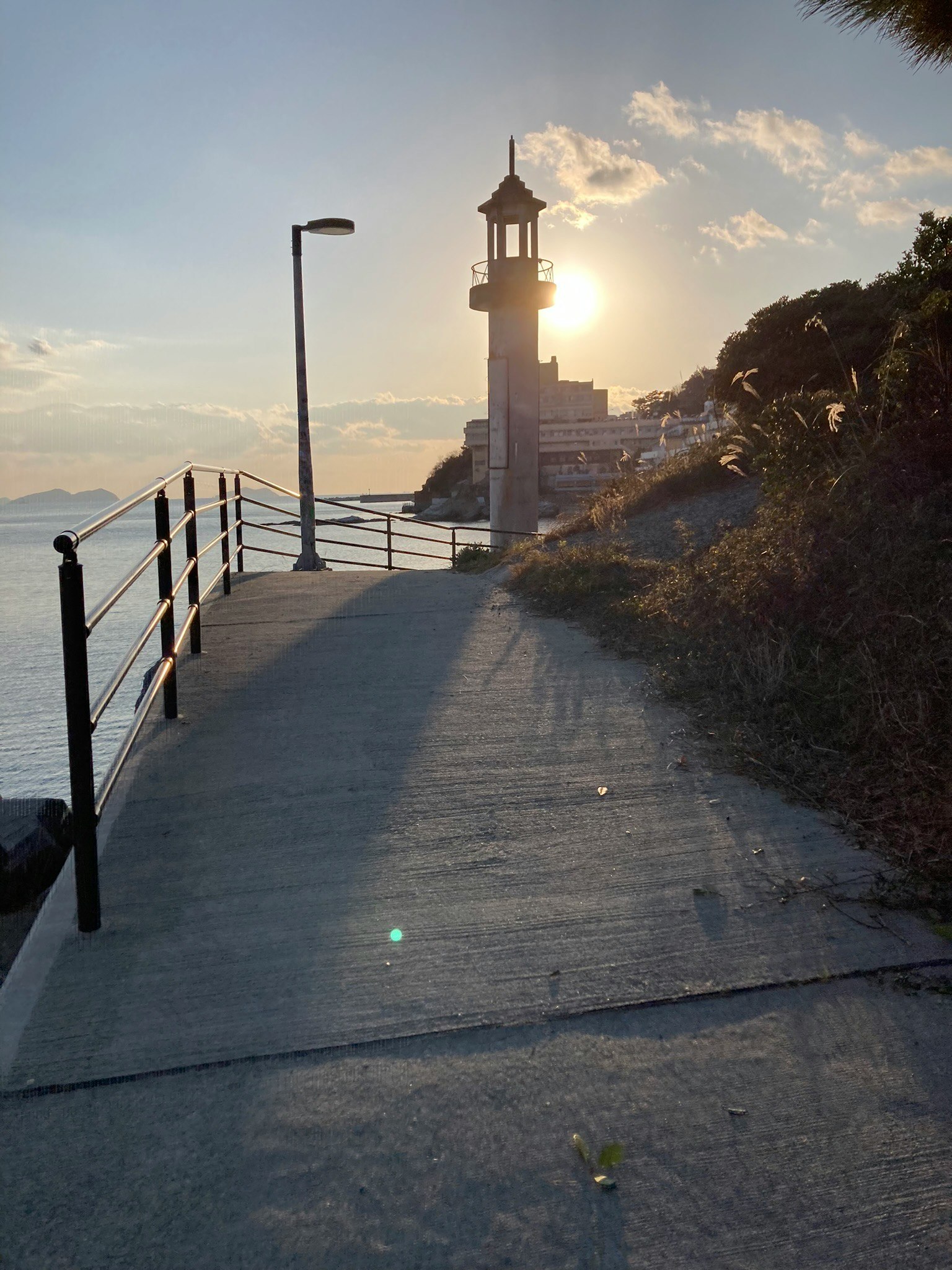 Coastal walkway with a lighthouse against the sunset