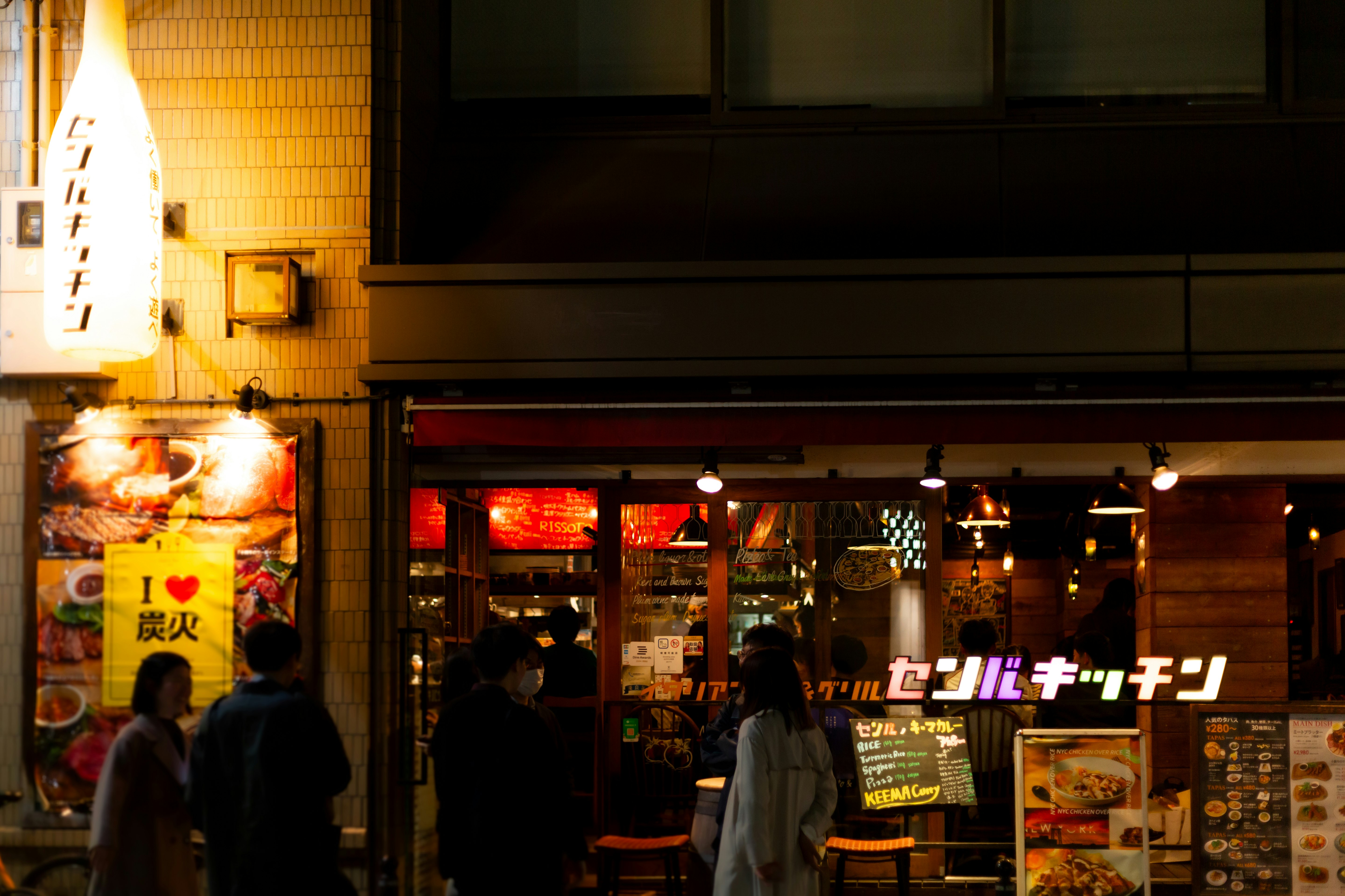 看板と提灯が並ぶ夜の飲食店街の入口