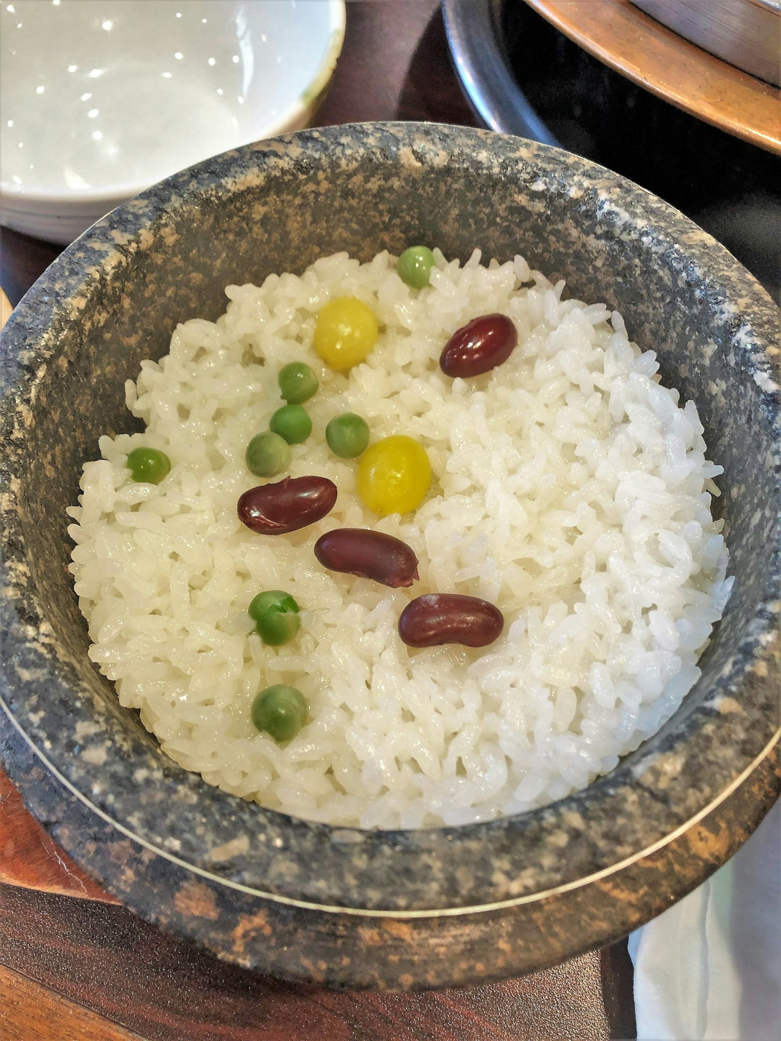 Arroz blanco servido en un tazón de piedra con guisantes verdes frijoles amarillos y frijoles rojos encima