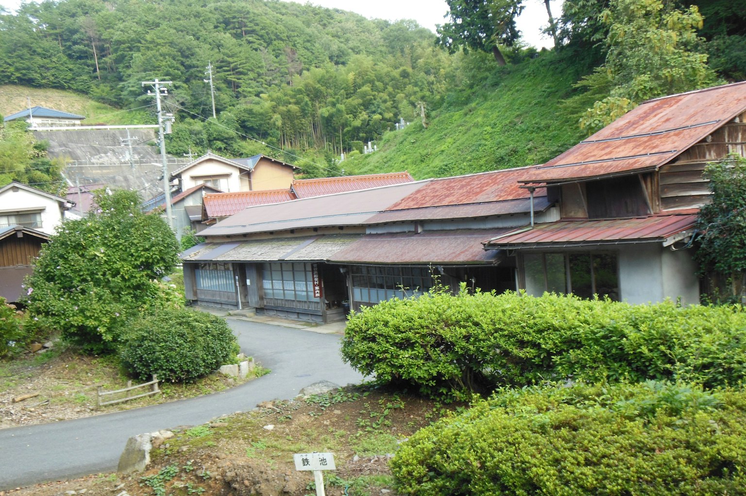 Rumah Jepang tua dikelilingi oleh pepohonan subur dan jalan berkelok-kelok