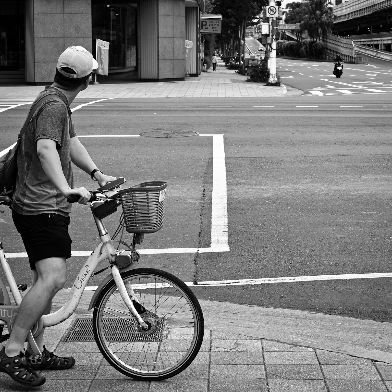 Un uomo in bicicletta che guarda un incrocio in una scena urbana in bianco e nero