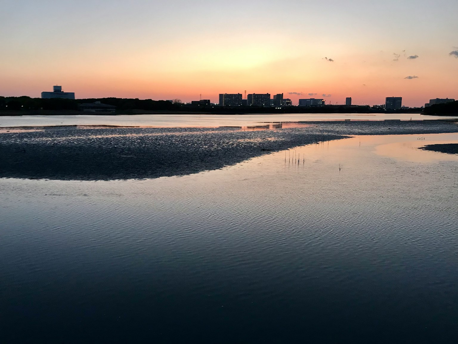 Ruhiges Wasser spiegelt den Sonnenuntergang mit städtischer Silhouette