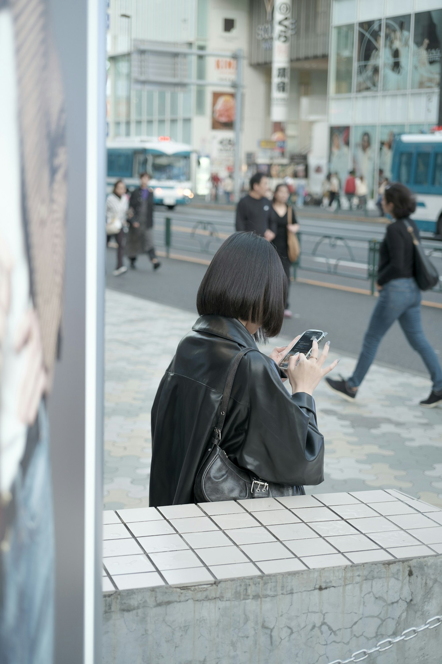 Woman using smartphone at street corner surrounded by pedestrians and urban scenery