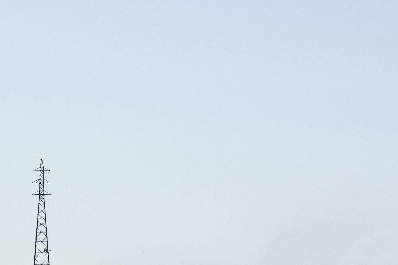 Silhouette di un palo elettrico contro un cielo blu chiaro