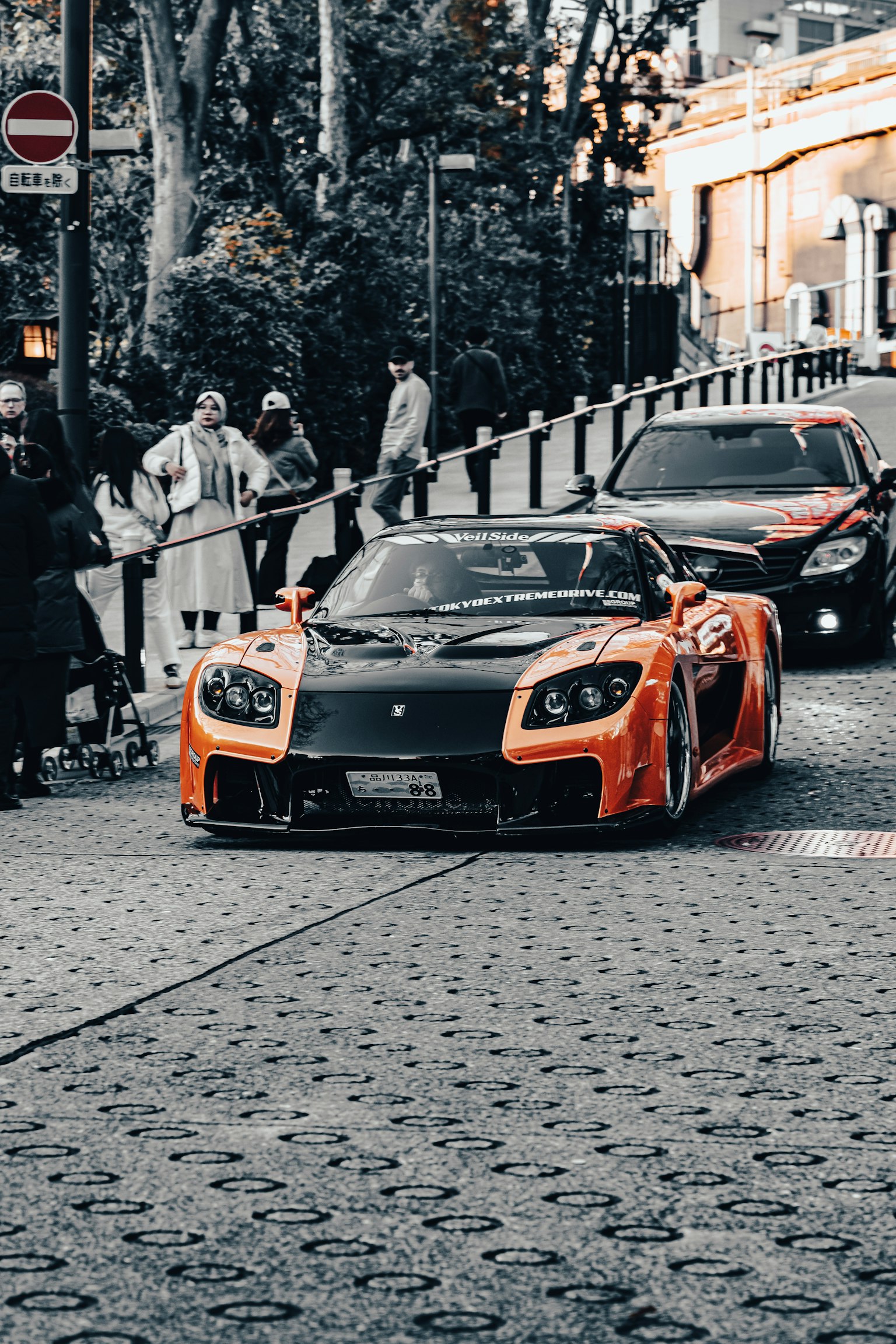 Auto sportiva arancione che attraversa la strada con spettatori