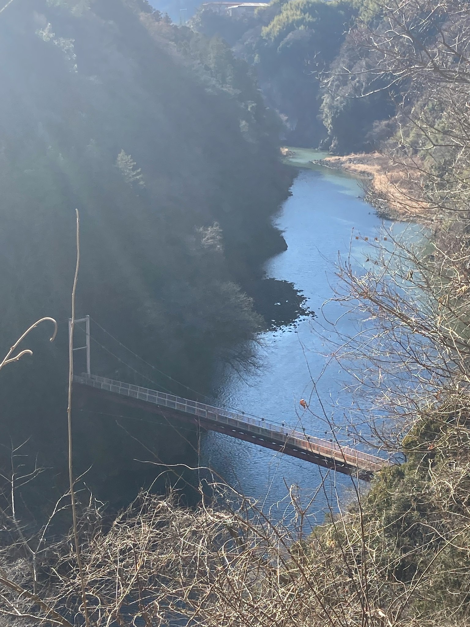 Vista escénica de un río azul con un puente colgante rodeado de colinas verdes y naturaleza