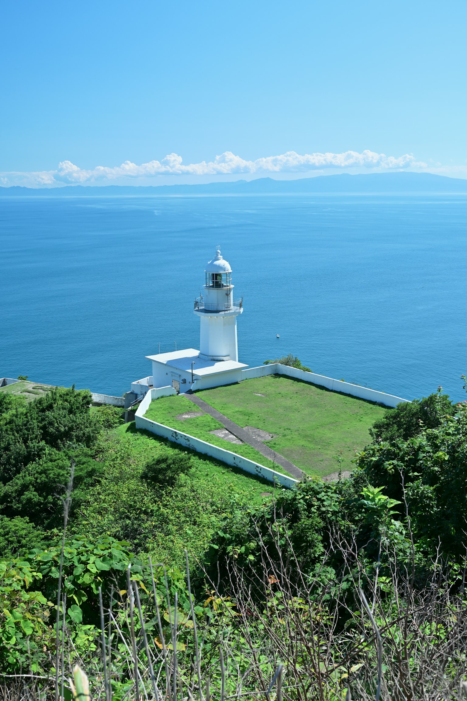 白色燈塔俯瞰藍色海洋的風景，綠草如茵