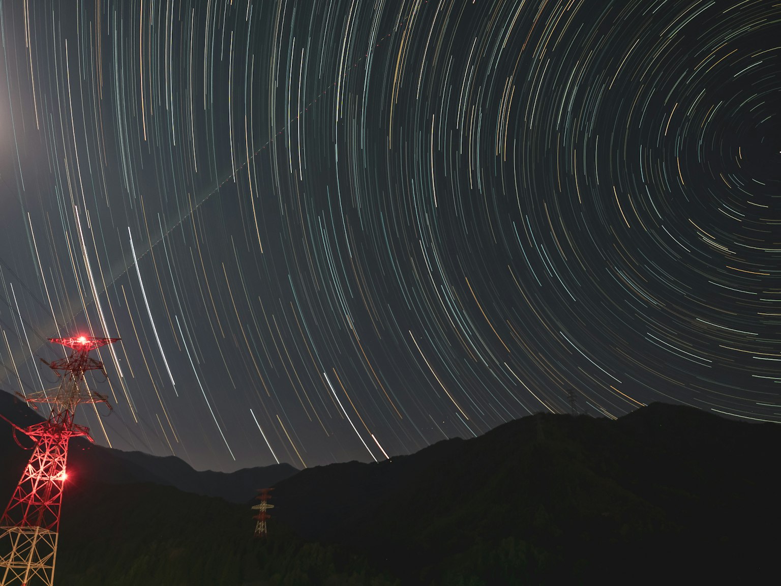Trajectoires d'étoiles avec silhouettes de montagnes et une tour radio