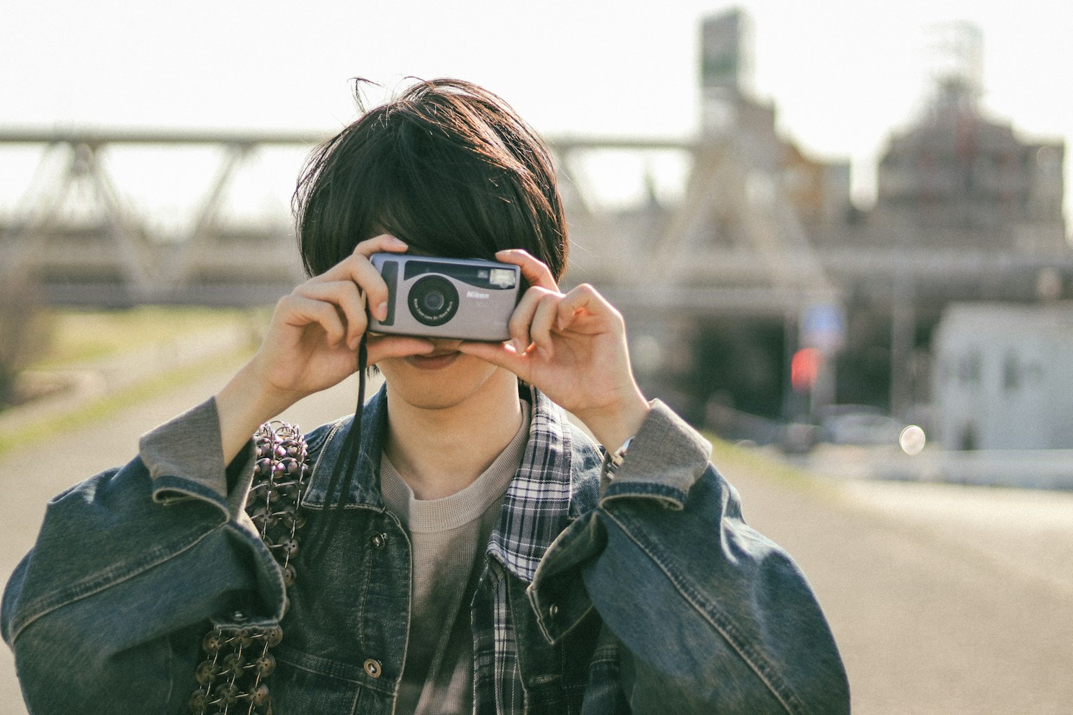 Un giovane con una macchina fotografica che posa contro uno sfondo di edifici industriali