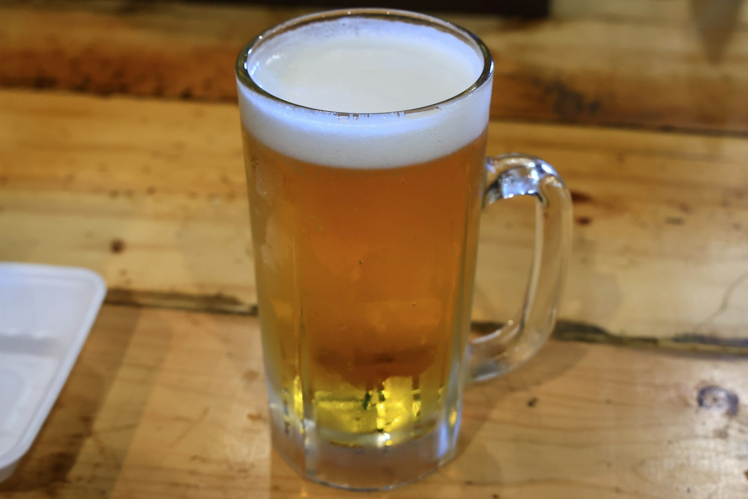 A clear beer mug filled with golden beer placed on a wooden table