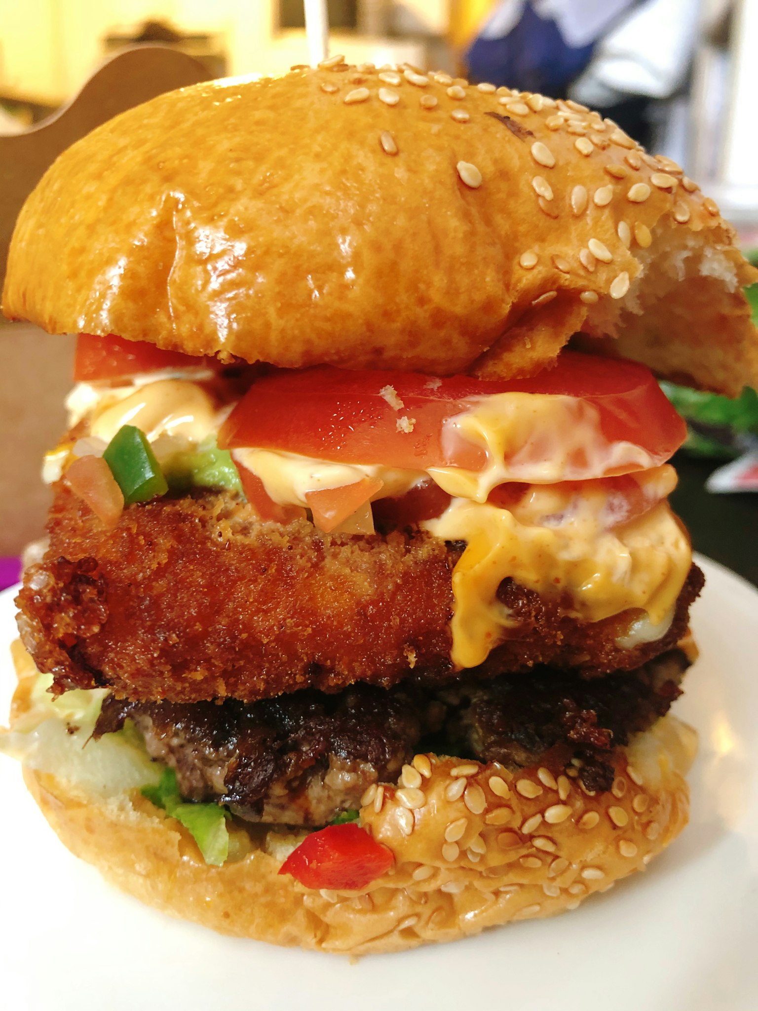 A towering burger featuring crispy chicken and juicy beef patty with fresh toppings