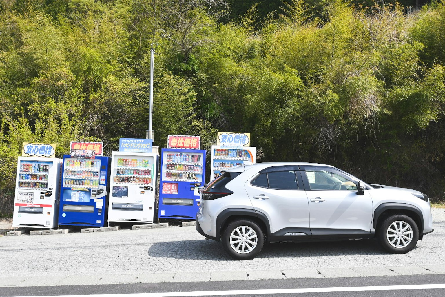 銀色汽車經過綠意盎然的自動販賣機
