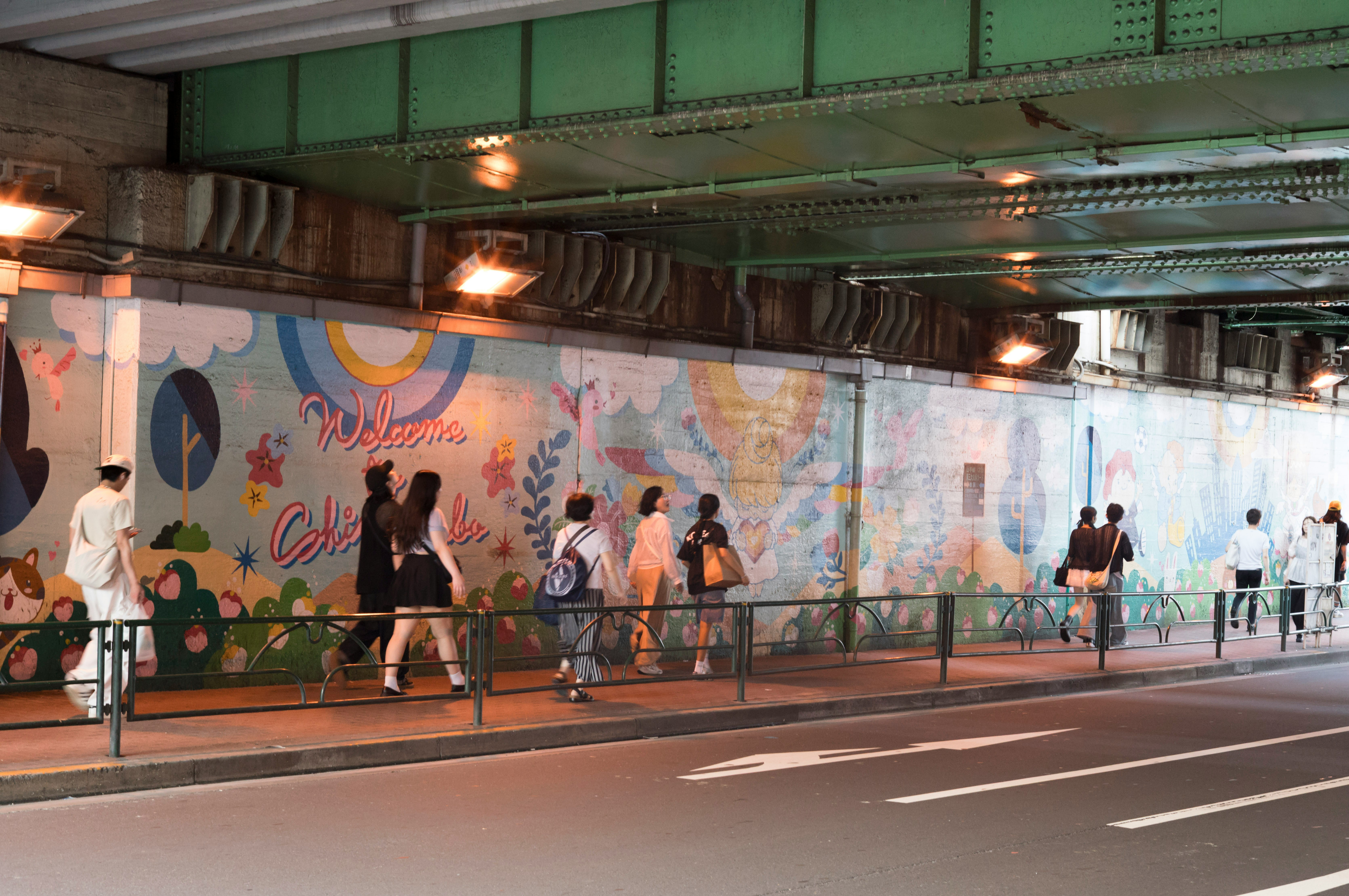 壁画のある高架下の歩道を歩く人々の風景