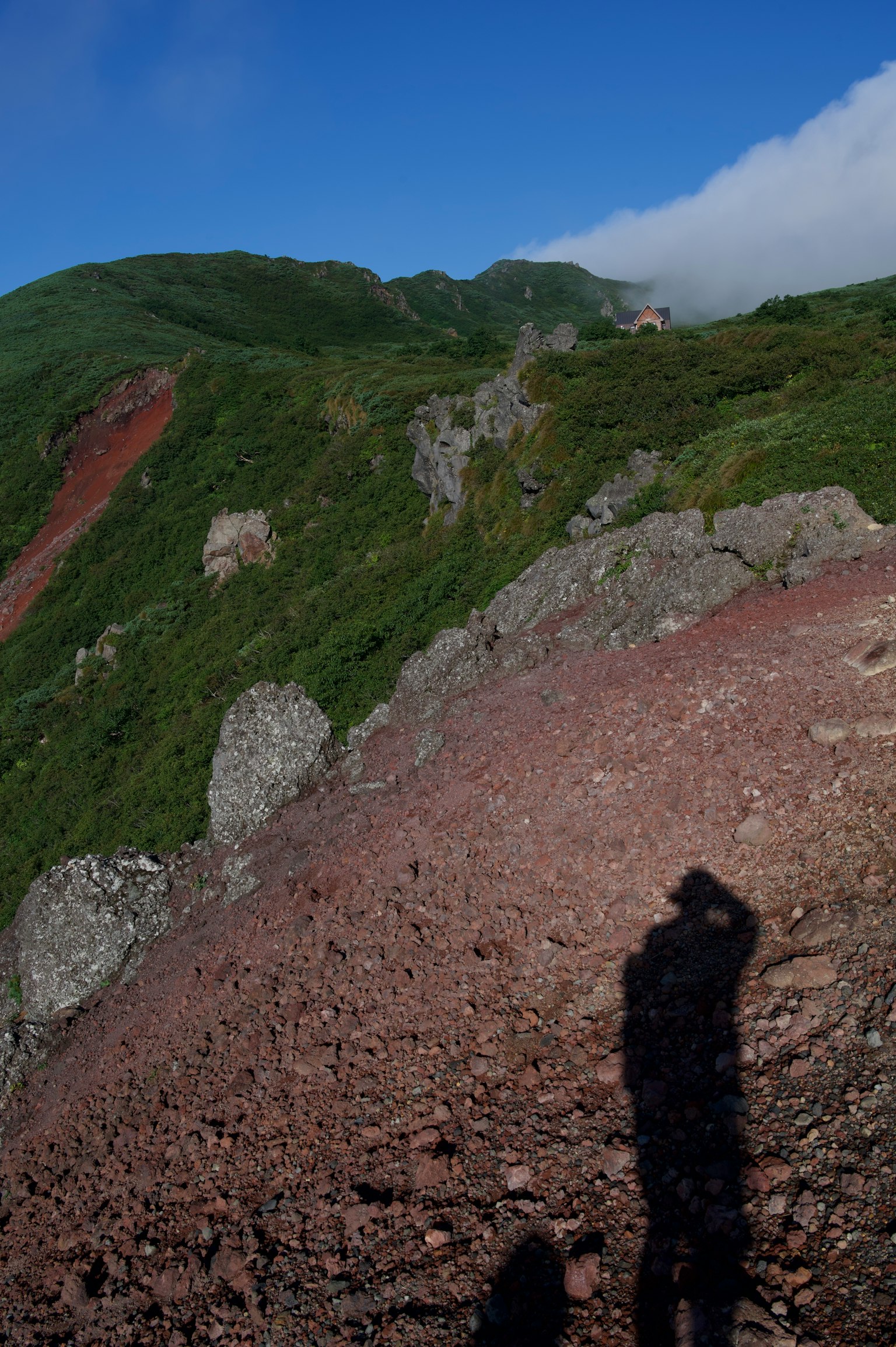 Bayangan seseorang di lereng berbatu dengan bukit hijau